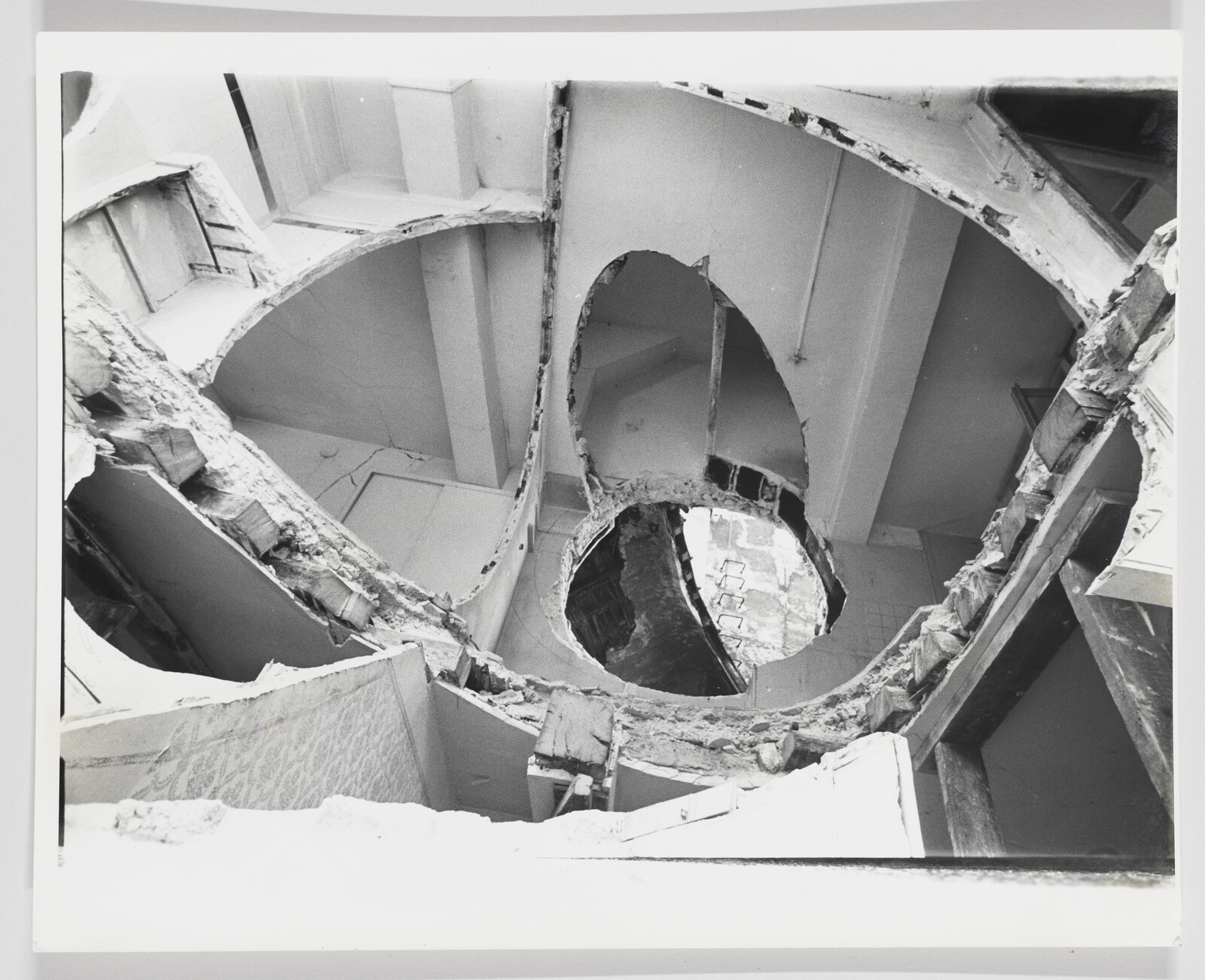 Multiple large circular holes cut through floors revealing exposed beams and debris inside a damaged building.