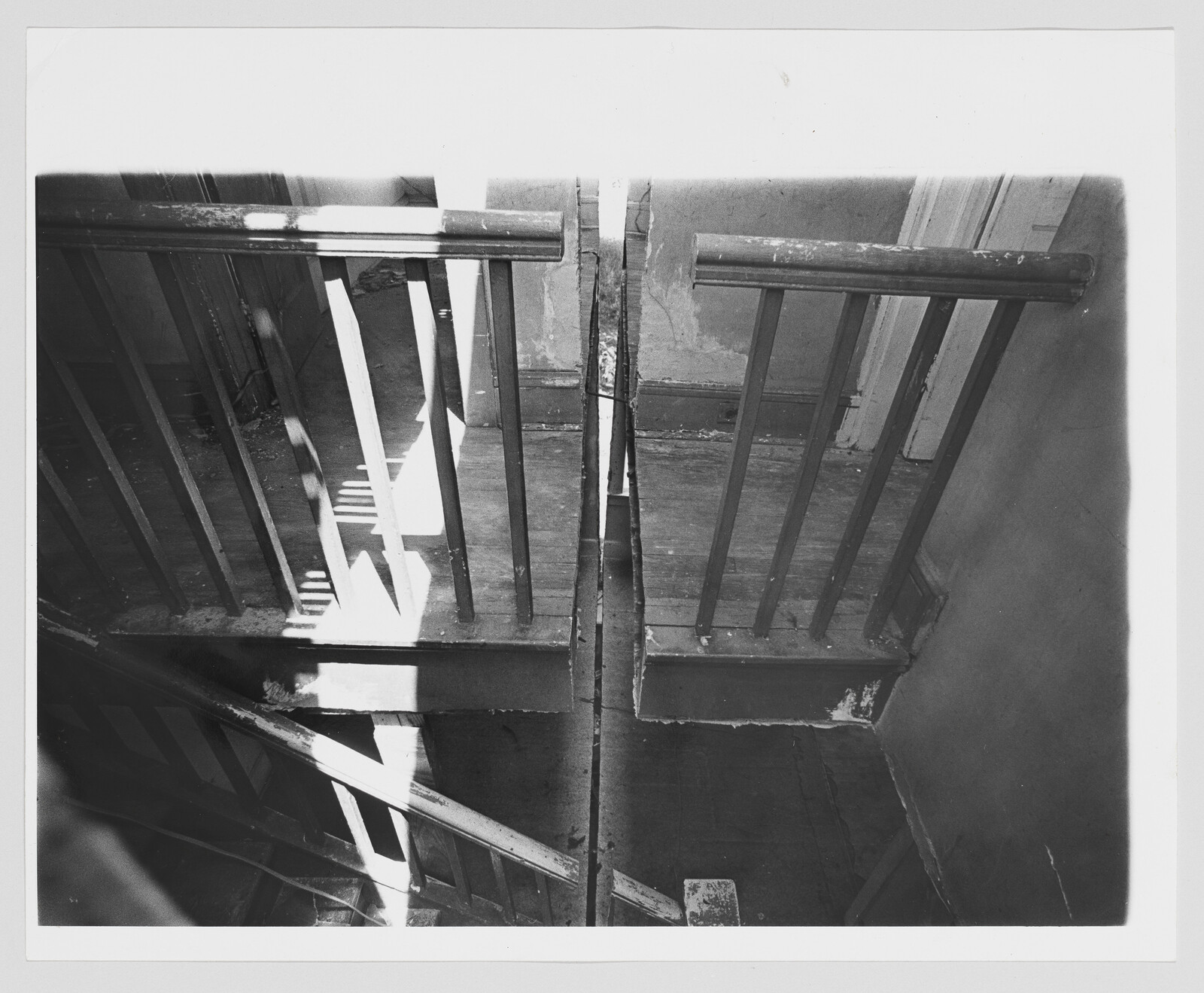 Split wooden stair landing with broken balusters and sunlight casting shadows across the stairs.