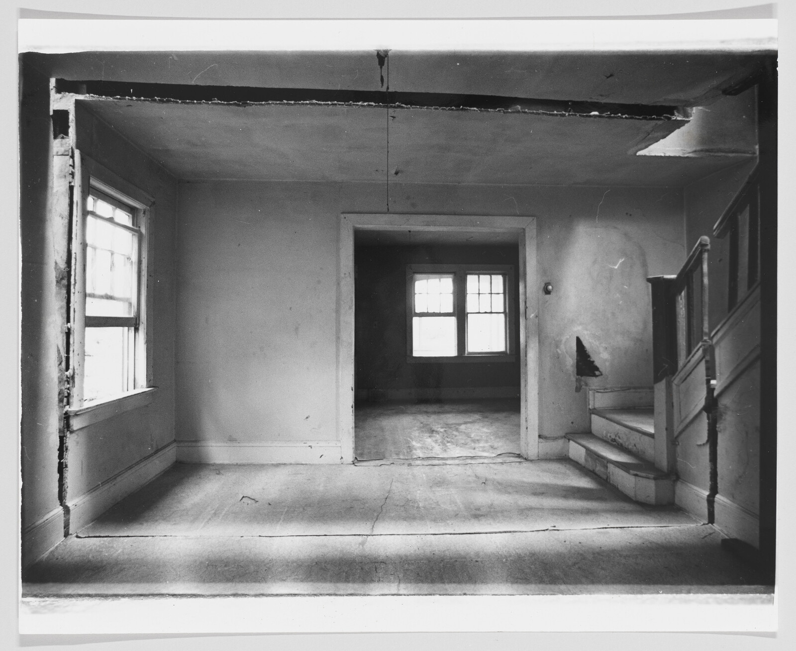 Empty room with worn floors, damaged plaster, and a small staircase leading up to the right.