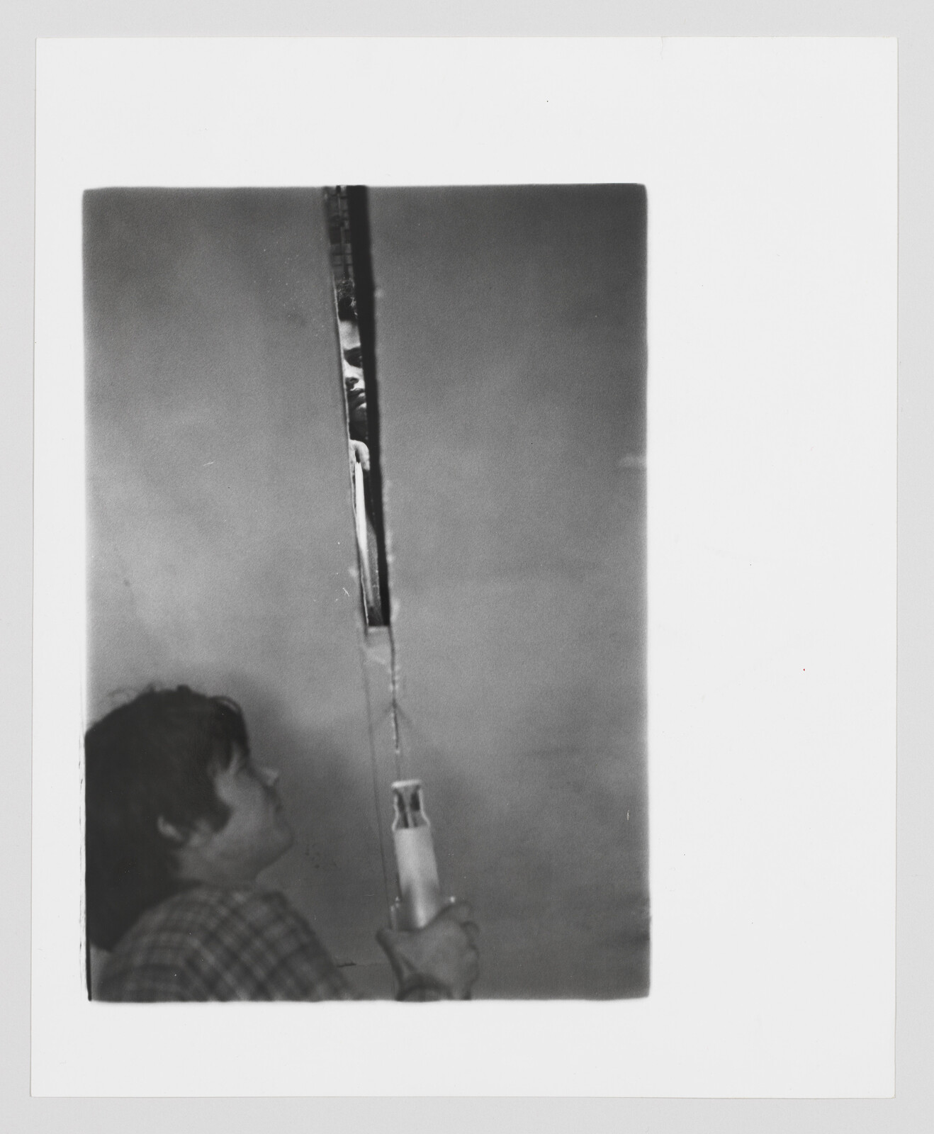 Child holds a long pole and looks up at a narrow slit where a face peeks through.