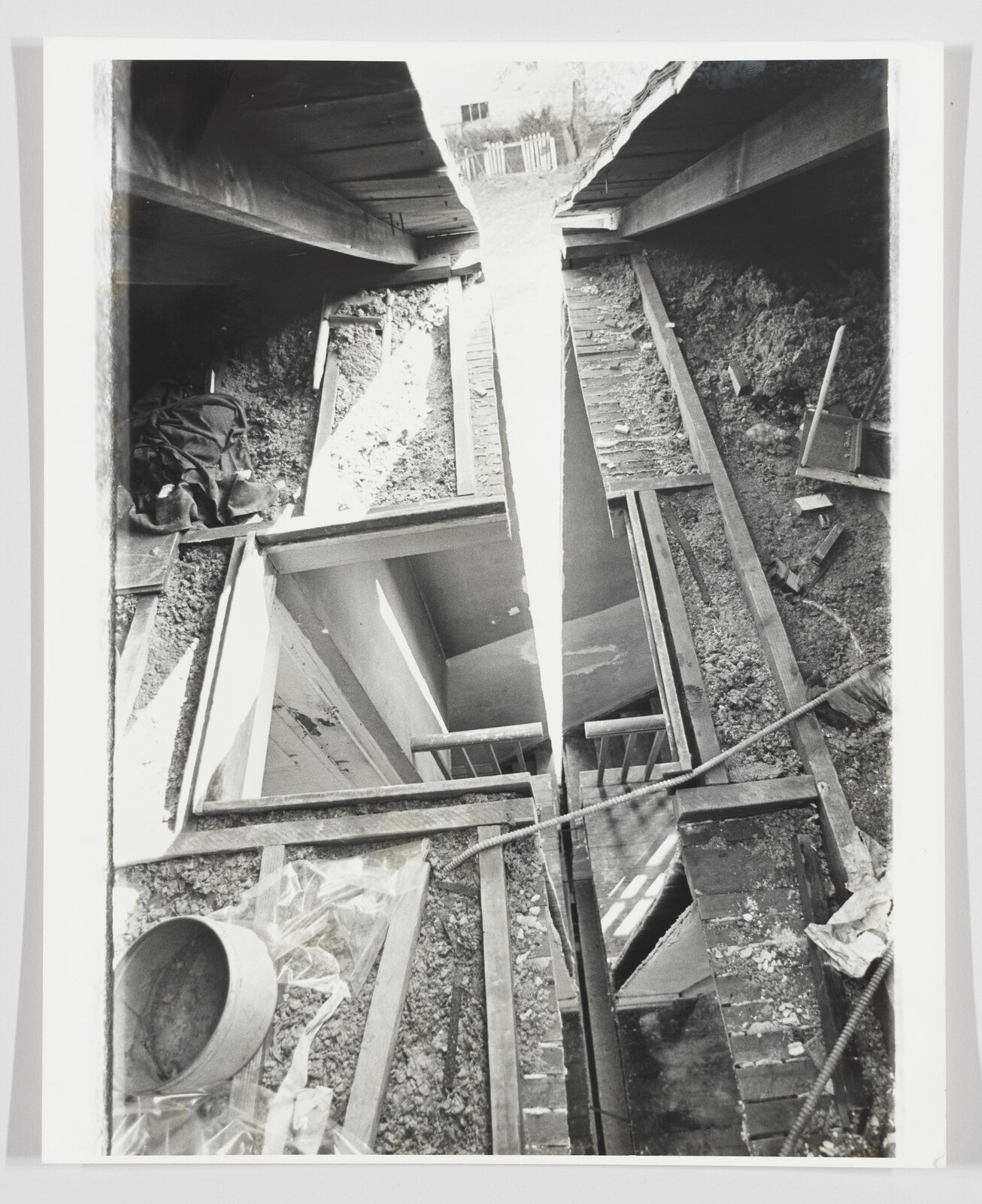 A collapsed floor reveals broken wooden beams and rubble around a deep vertical shaft.