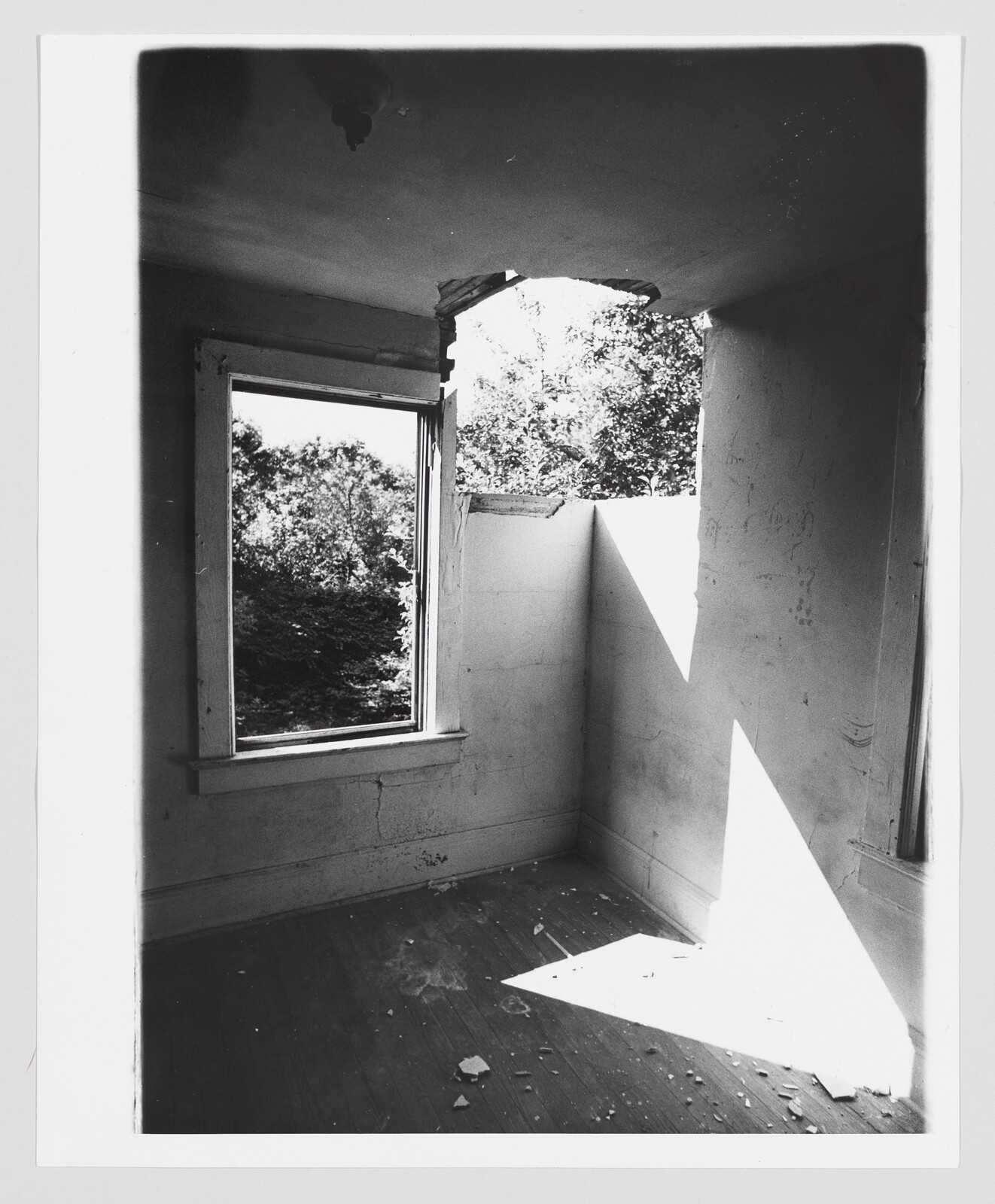 Empty damaged room with a large hole in the ceiling casting a triangular patch of sunlight.