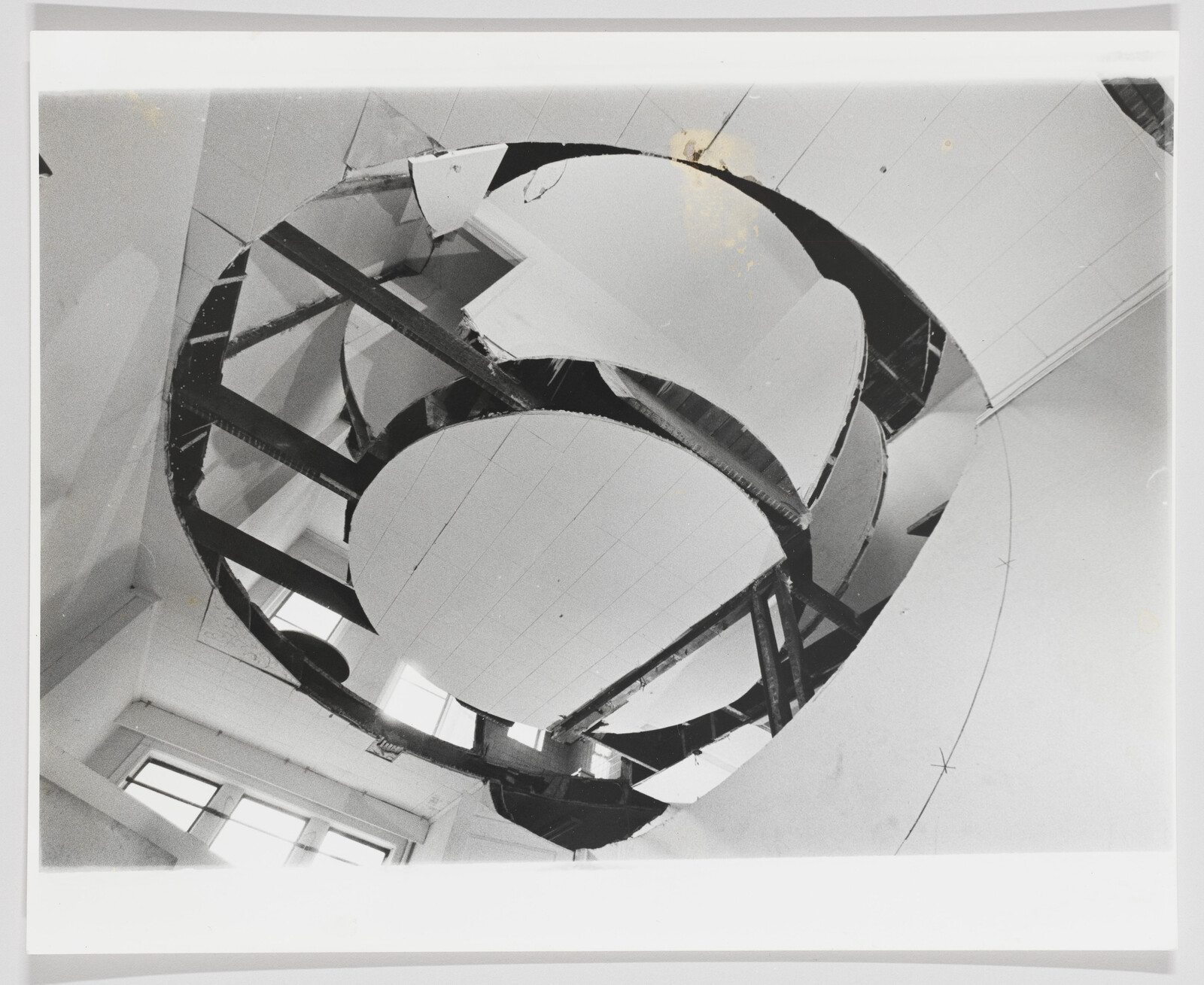 A large circular ceiling opening reveals exposed metal beams and broken panels above a room.