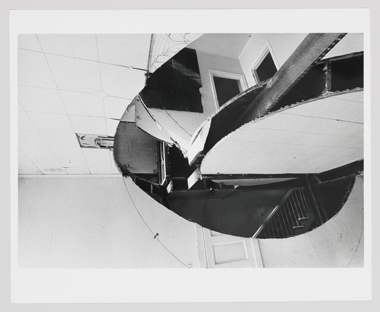 Black and white photograph depicting a distorted view of a building, with curved and fragmented sections creating an abstract composition against the sky.