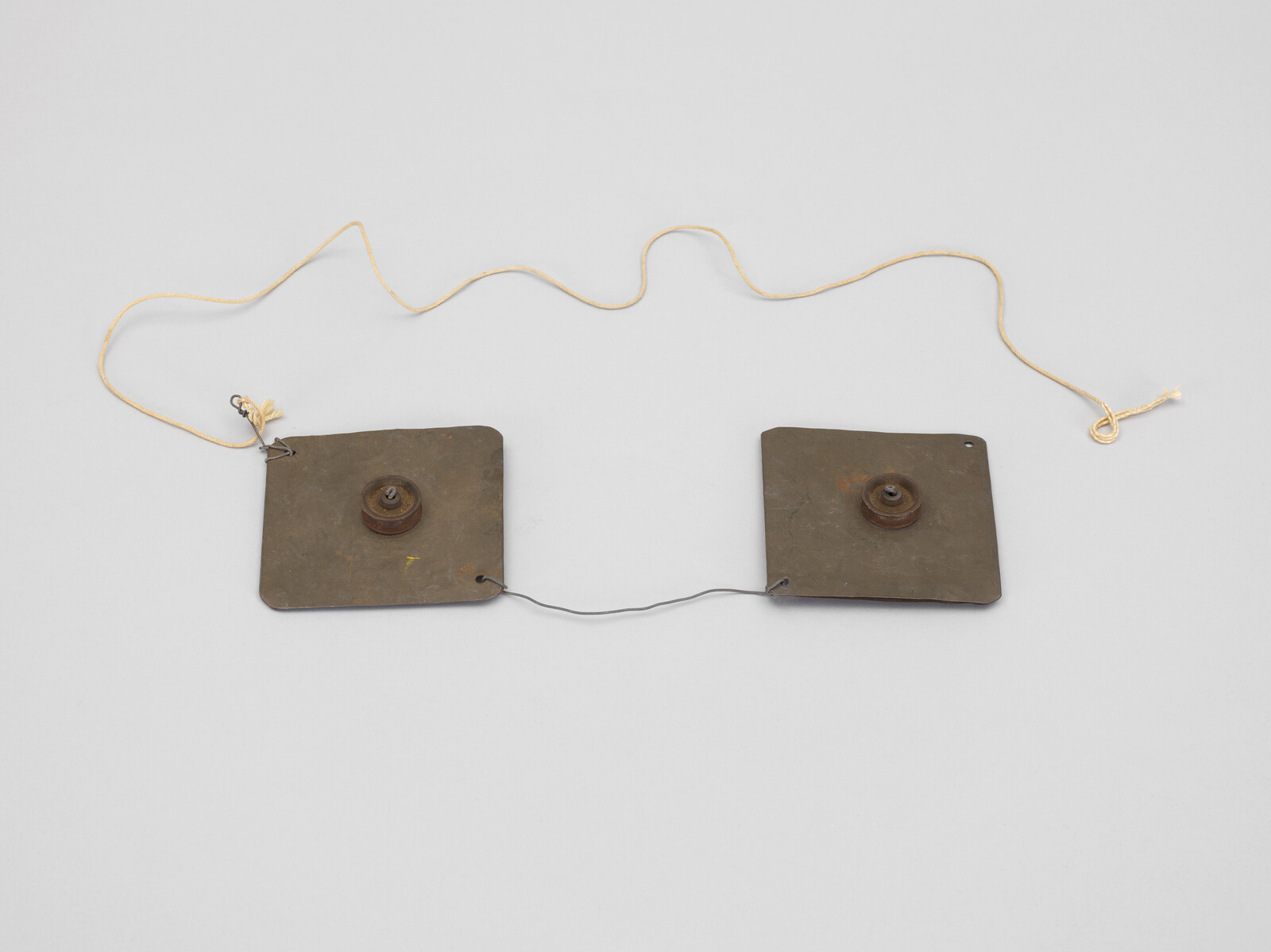 Two square metal plates connected by a short wire with a long yellow cord attached.