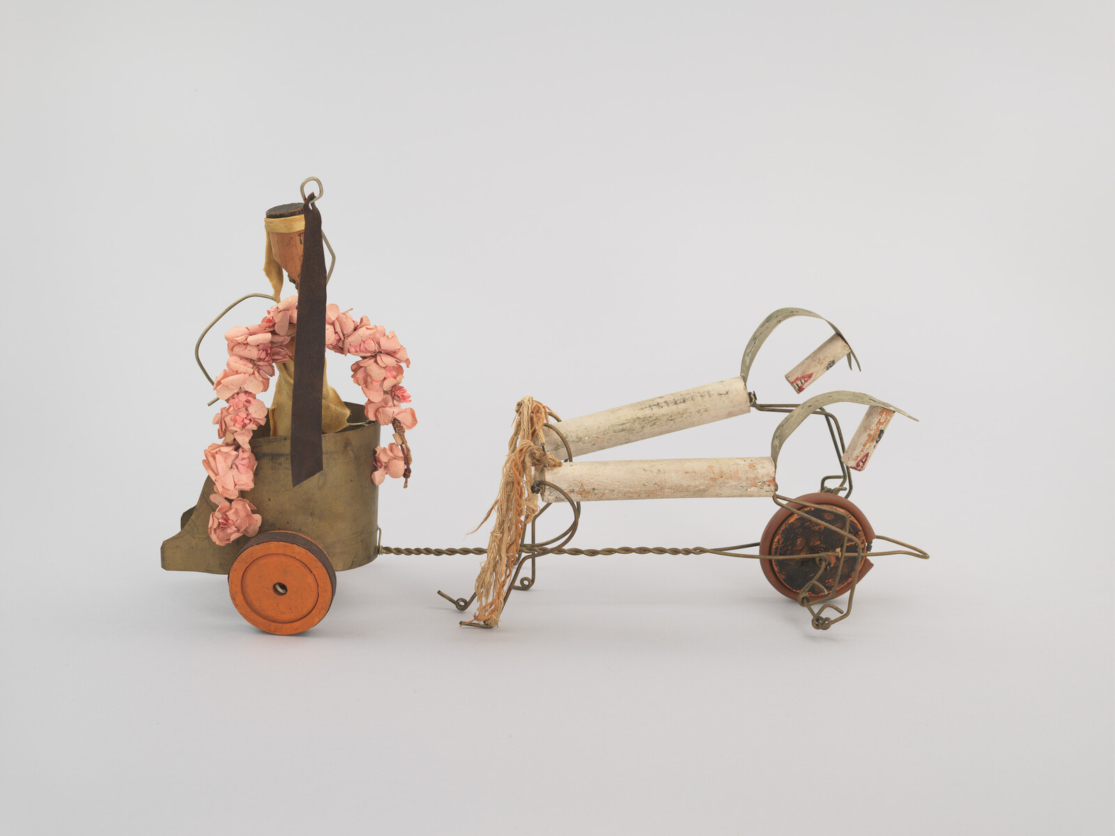 A whimsical sculpture with wheels, pink flowers, and metal parts, resembling a small cart or vehicle.