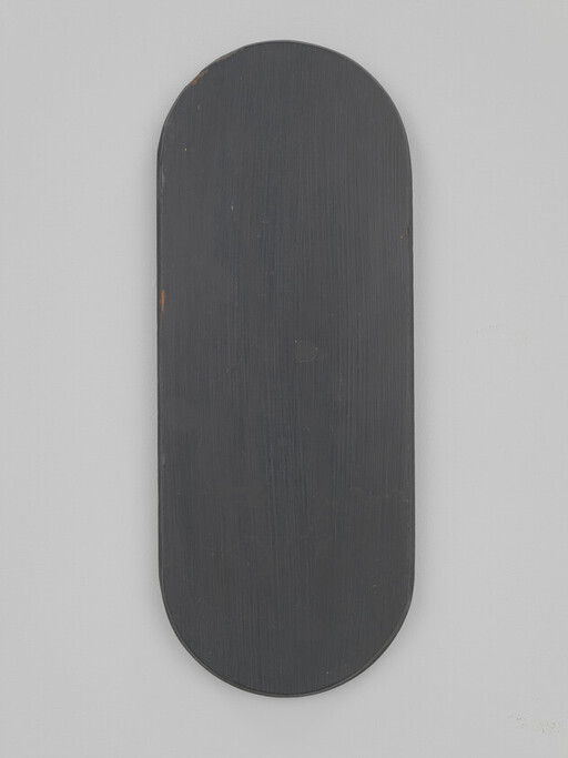 Long narrow rounded black wooden panel mounted vertically on a light gray wall.