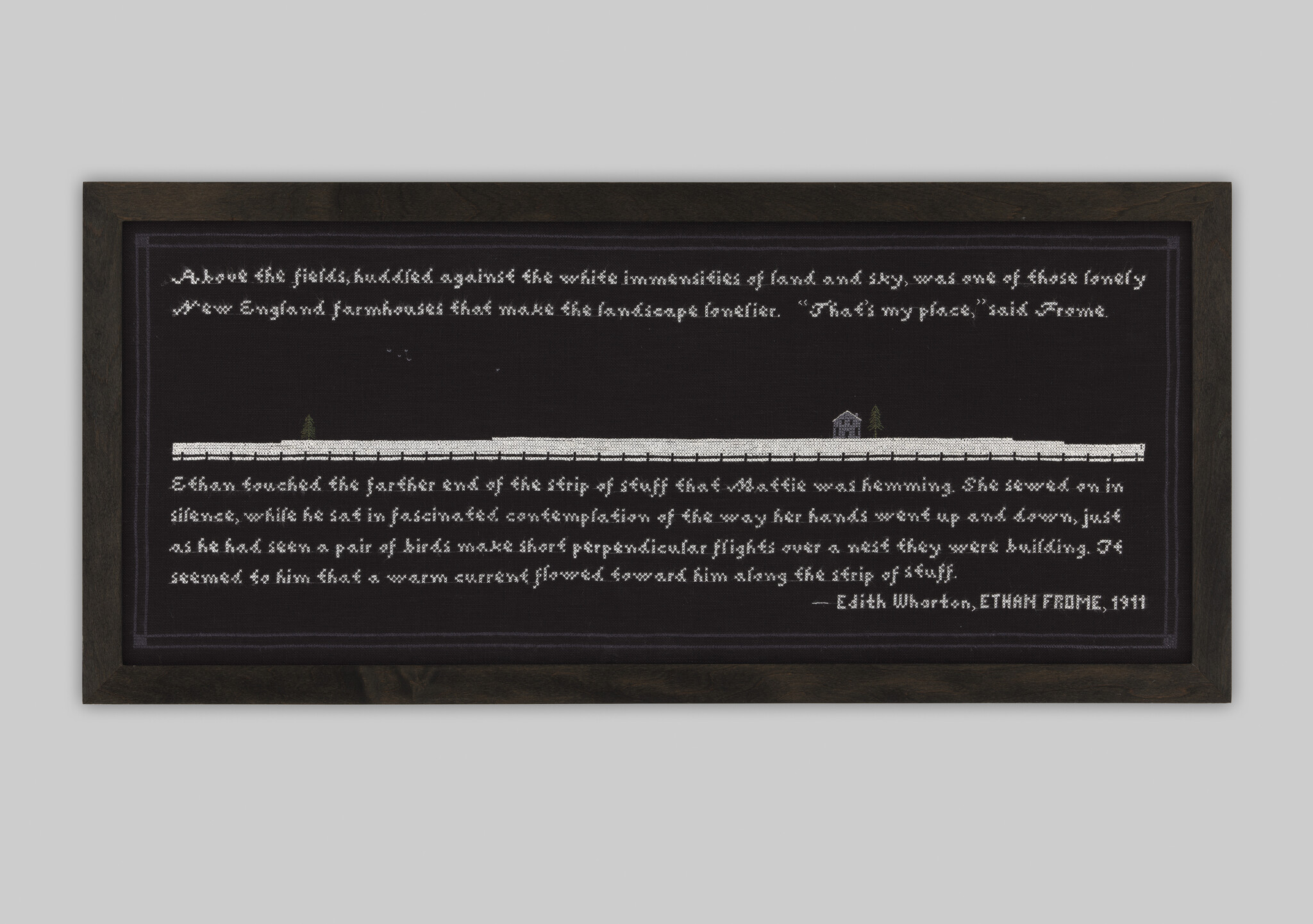 Framed black textile artwork with white stitched text and a small house and fence motif.