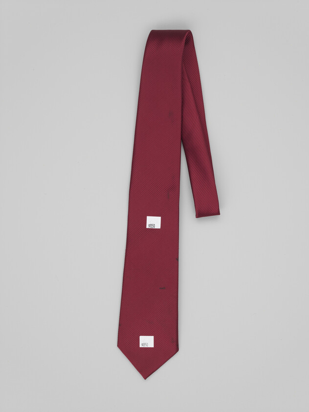 A plain maroon silk necktie laid flat against a light gray background.