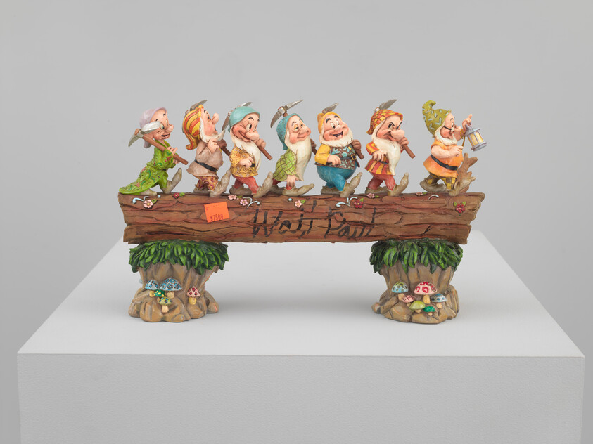 Seven small dwarfs wearing colorful clothes march across a carved wooden log bench display.