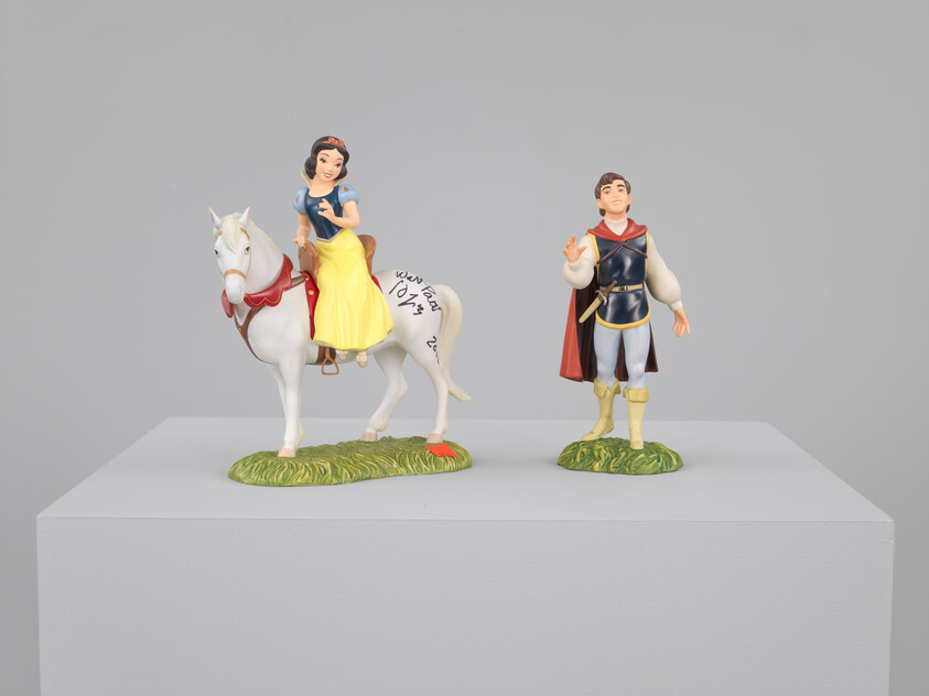 Snow white figurine rides a white horse while a prince figurine stands beside her.
