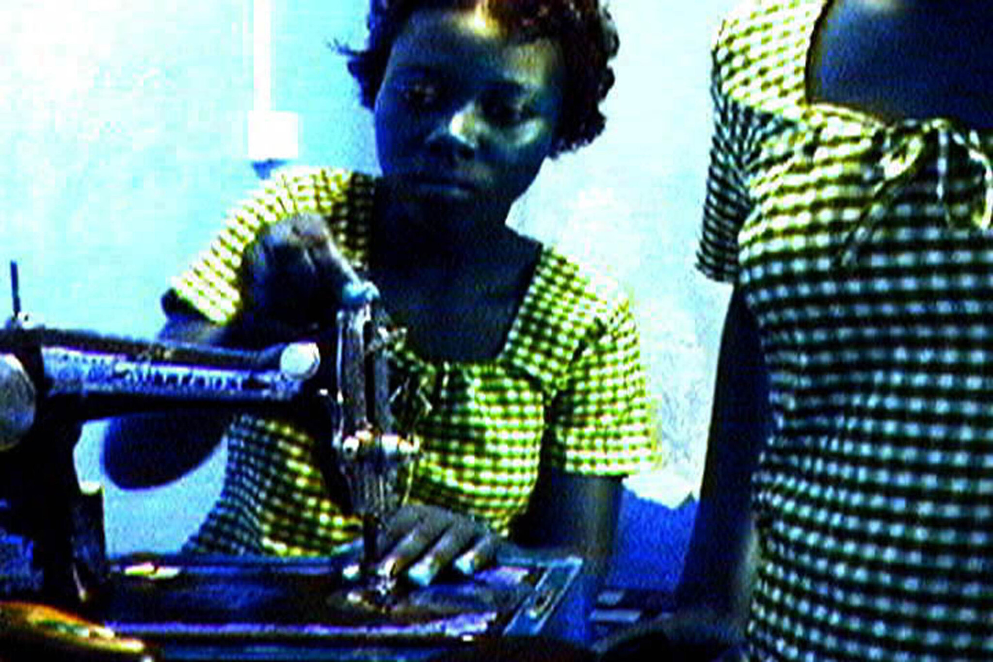 Young woman wearing a checkered dress using a sewing machine to stitch fabric.