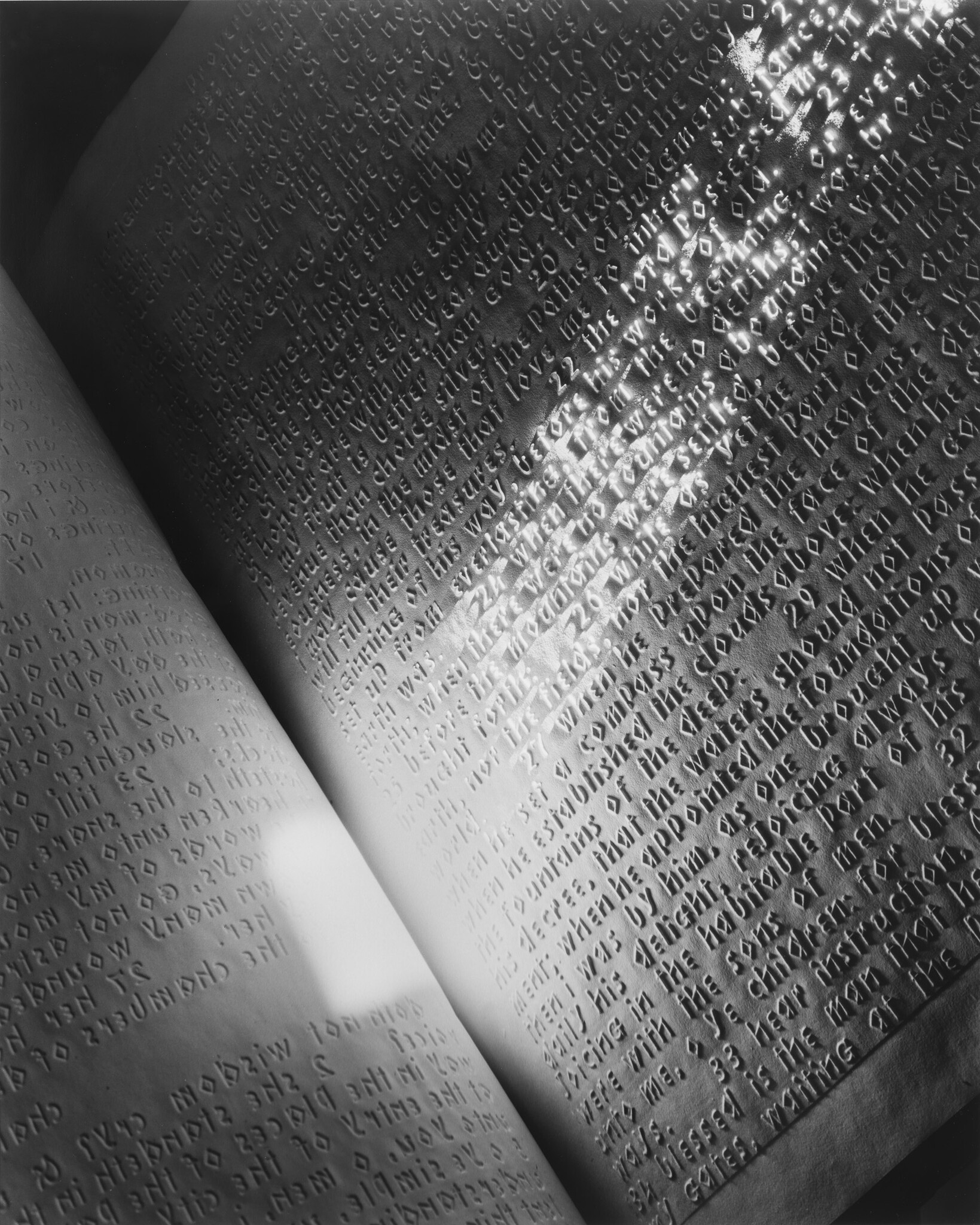 Open book pages embossed with raised tactile text illuminated by a bright diagonal light reflection.