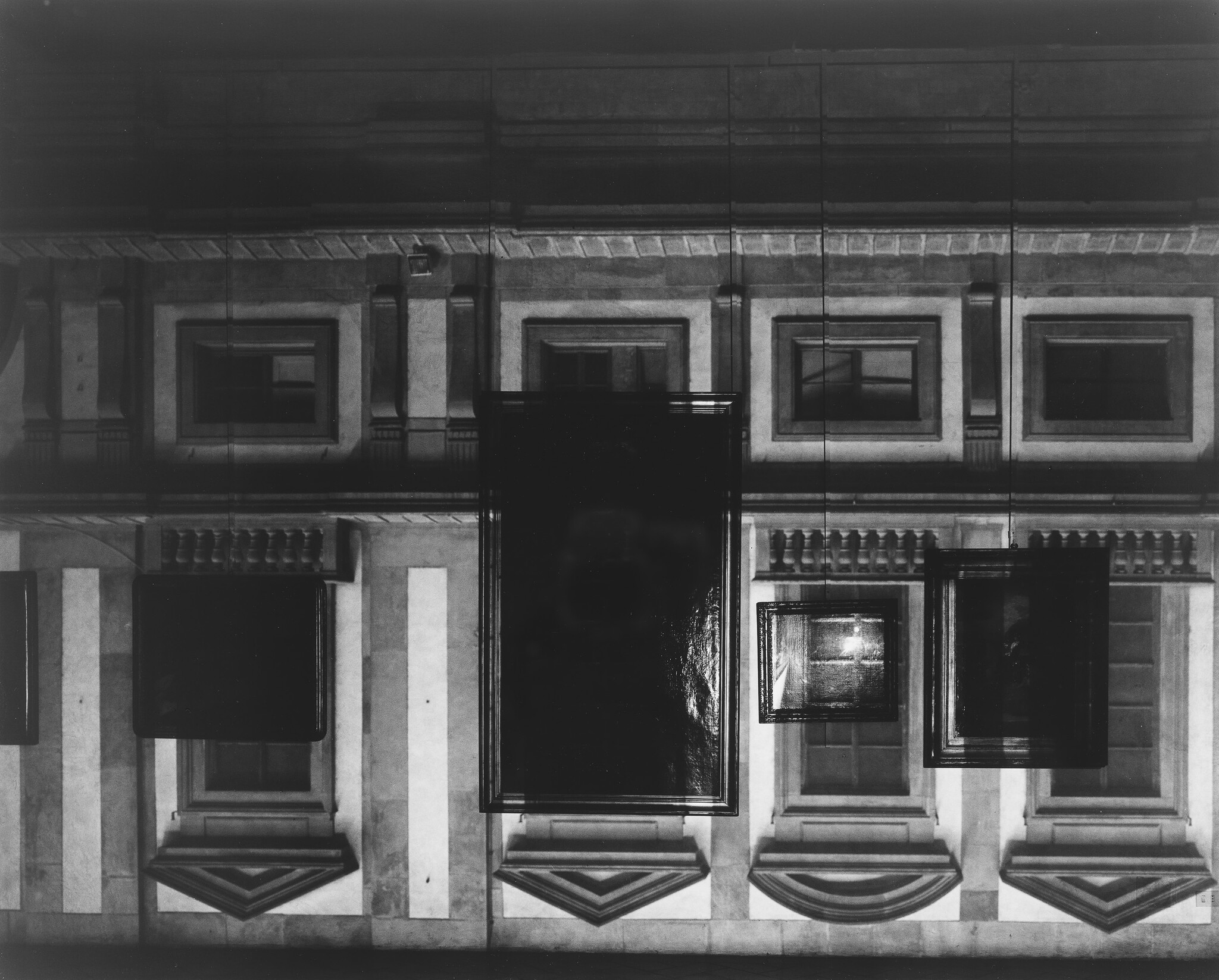 Large dark framed paintings hang in front of a classical building facade at night.