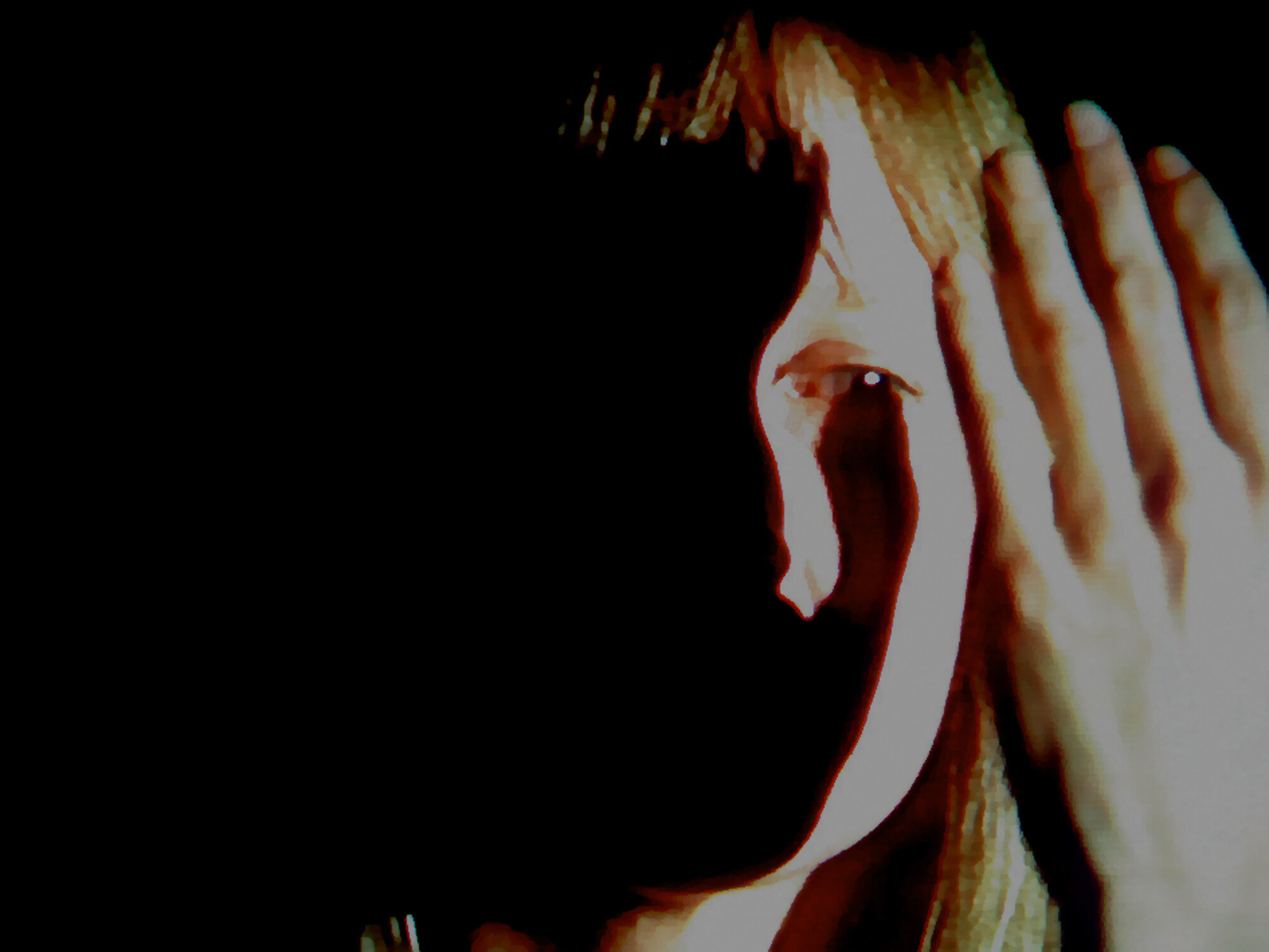 A person holds their hand to the side of their face, one eye visible in shadow.