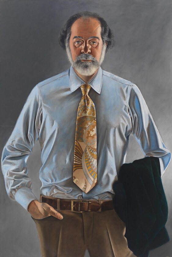 Bearded man wearing a patterned tie and holding a dark jacket while standing with one hand in his pocket.