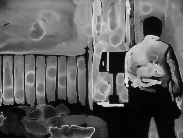 A person stands with their back to the camera beside a railing and a mailbox.