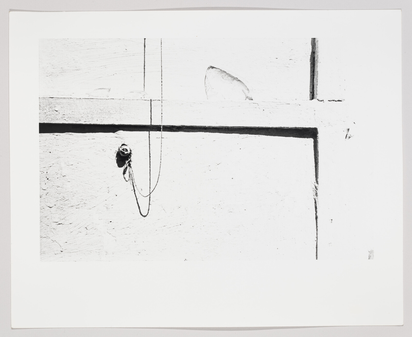 A black-and-white wall with a small hook and a looped cord hanging from a horizontal beam.