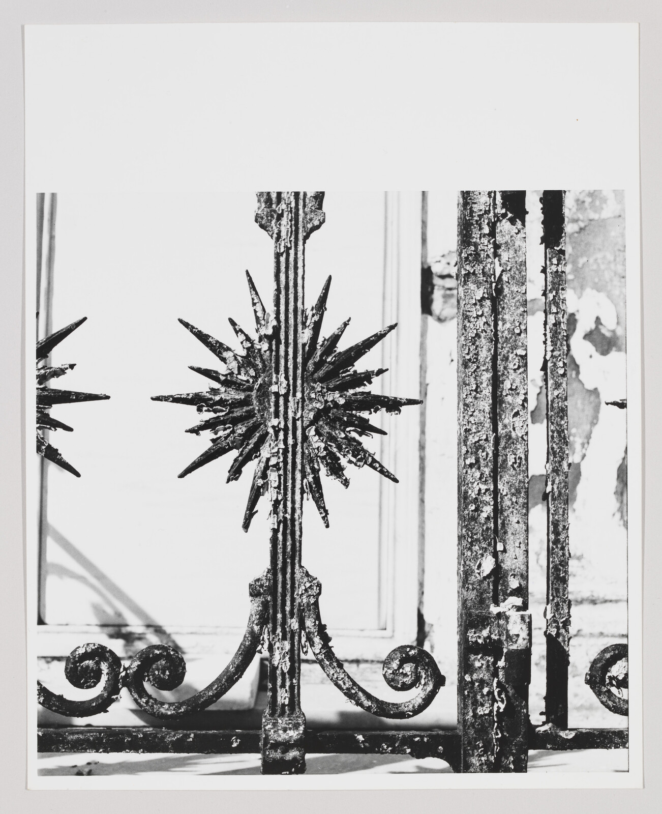 Rusted wrought-iron gate with spiky starburst ornament and peeling paint on vertical bars.