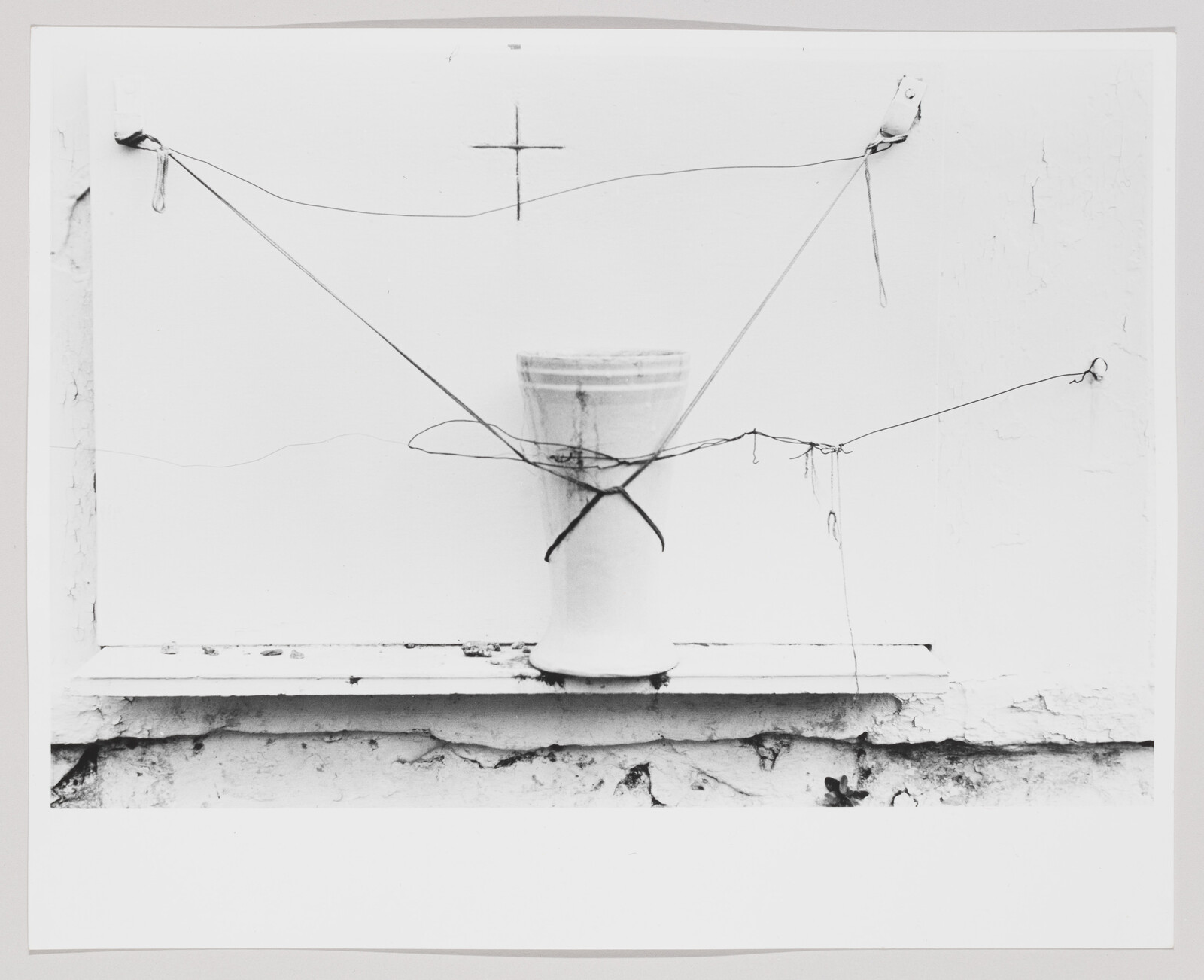 A ceramic vase on a windowsill is tied with crisscrossing wires and strings.