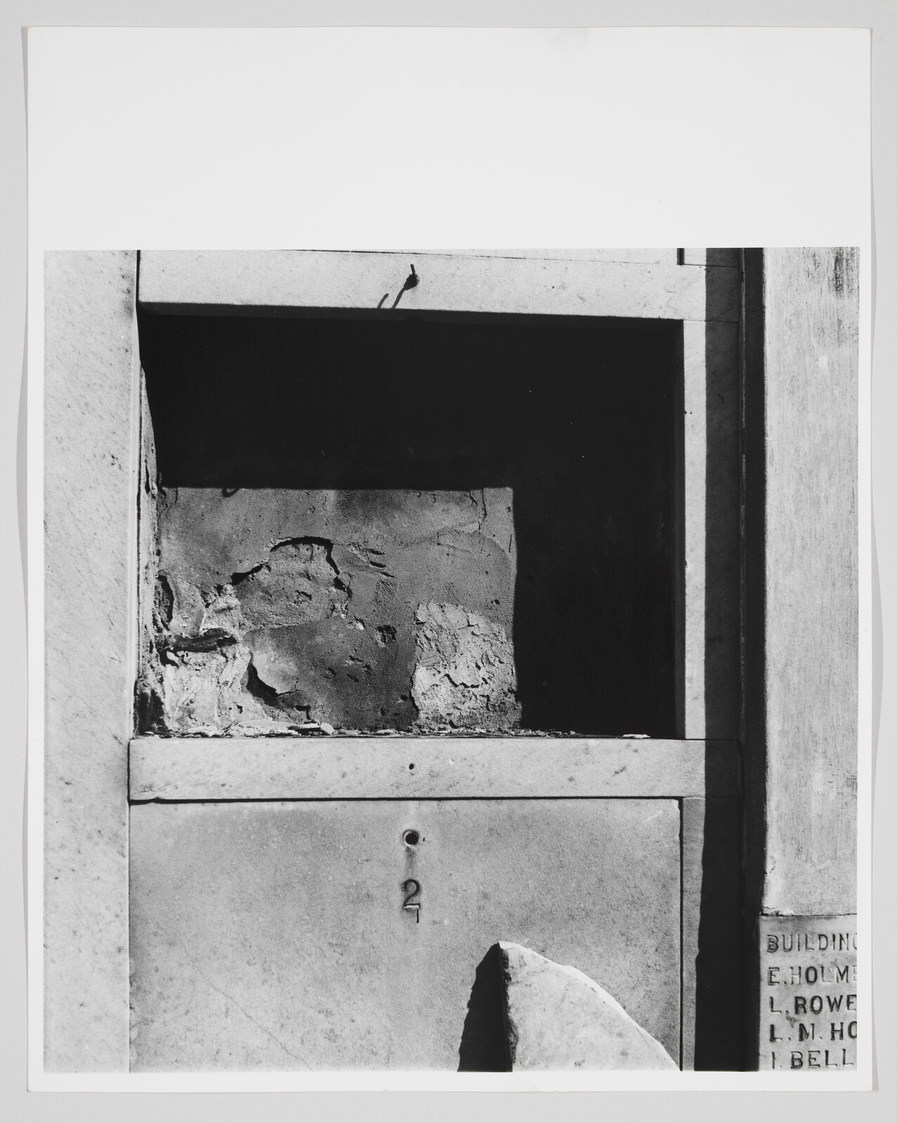 A weathered stone niche with peeling plaster and a small metal number 2 on its front.