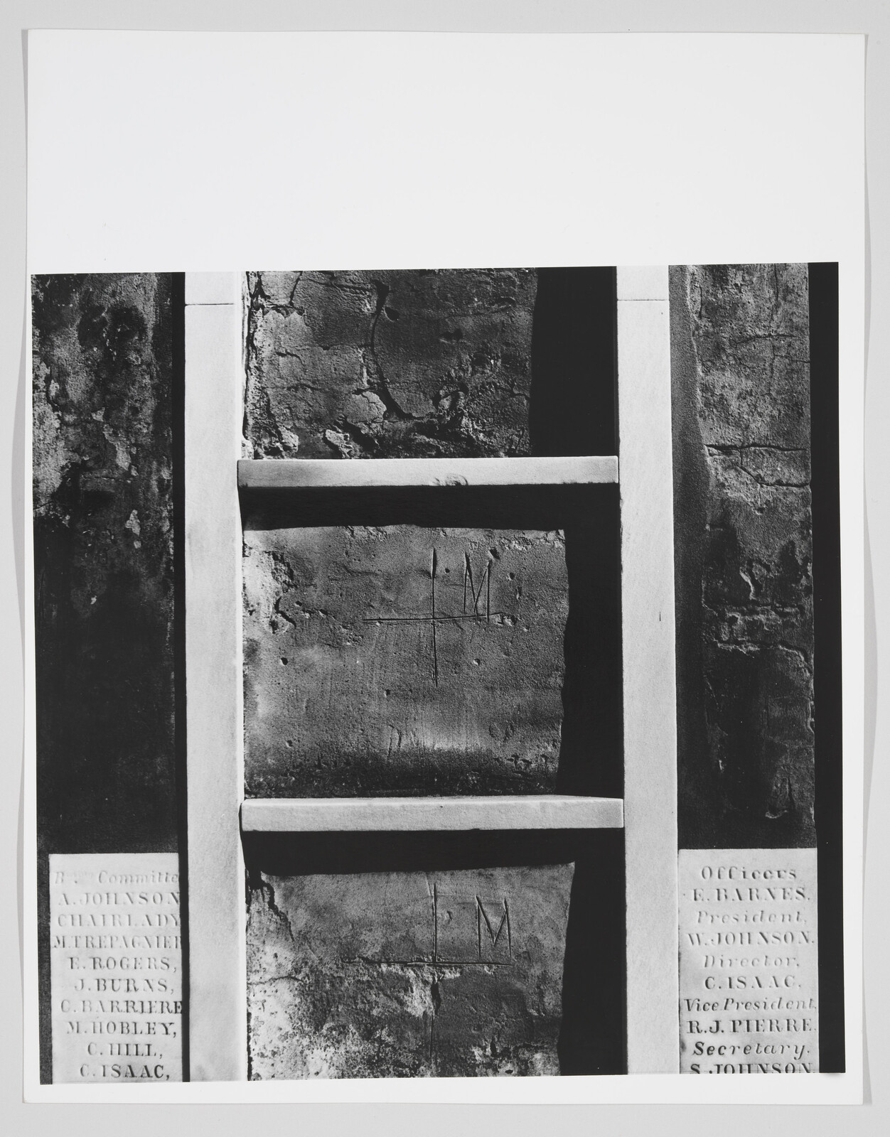 White wooden ladder-like frame against cracked plaster wall with carved initials and name plaques.