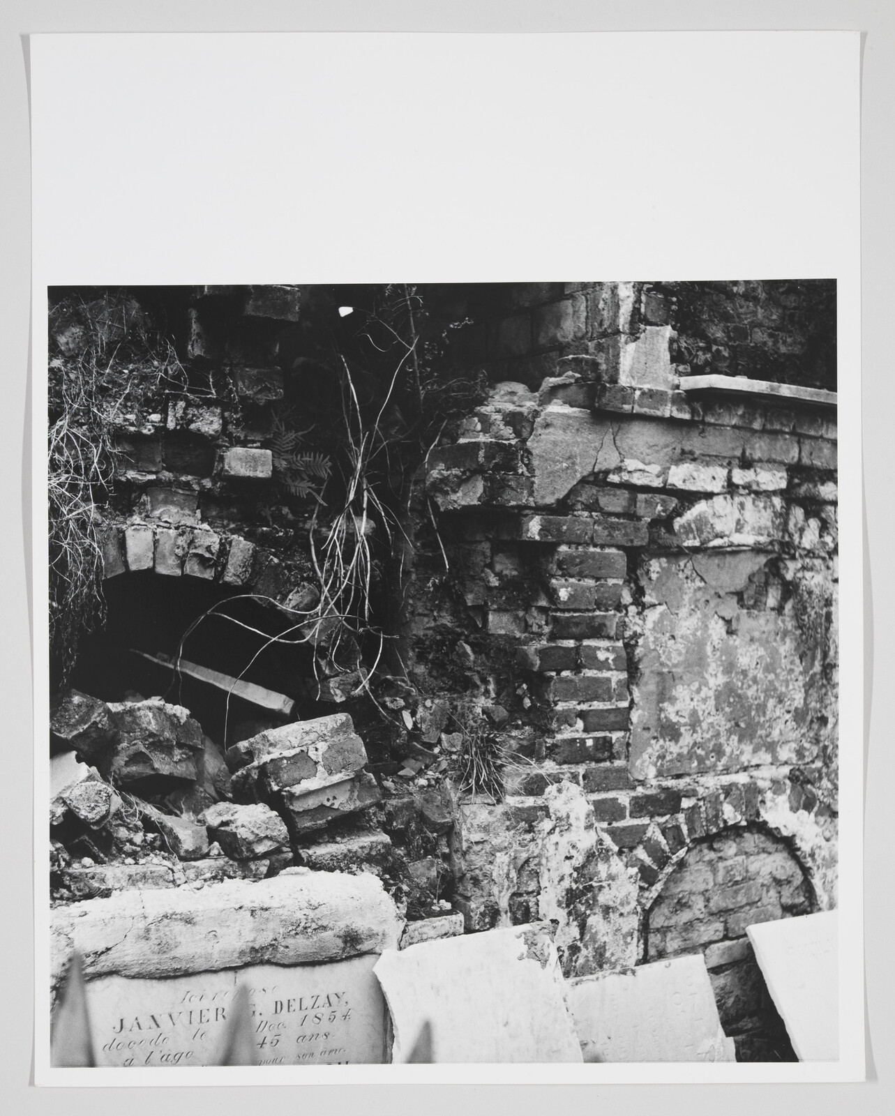 Crumbling brick wall with collapsed masonry, tangled roots, and broken gravestones leaning in front.