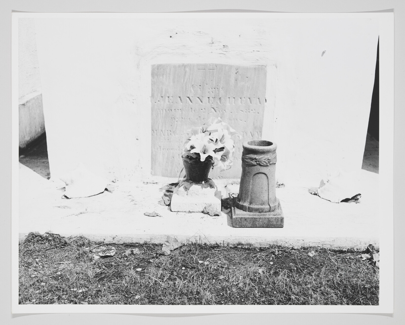 A small grave marker with a pot of lilies and a stone vase placed on the tomb.