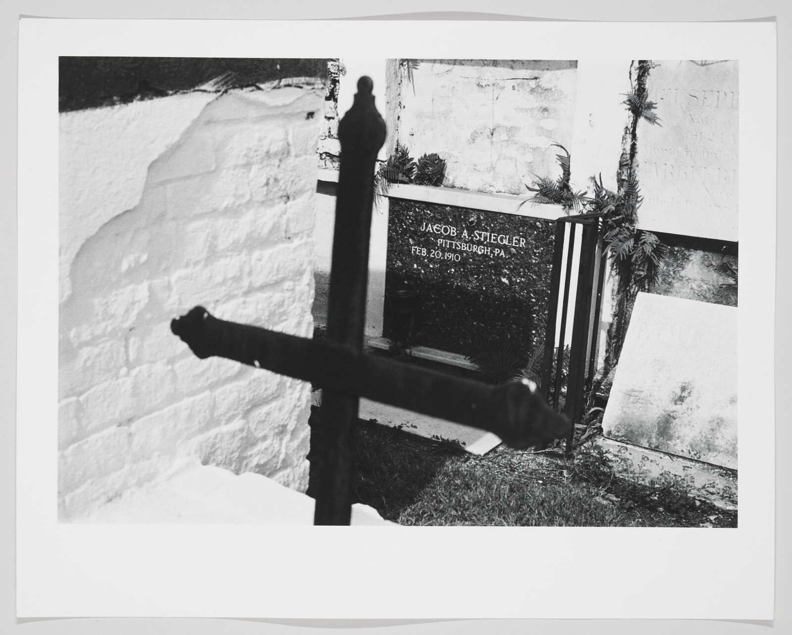 Wrought-iron cross silhouette in front of Jacob A. Stiegler's cemetery marker dated Feb. 20, 1910.