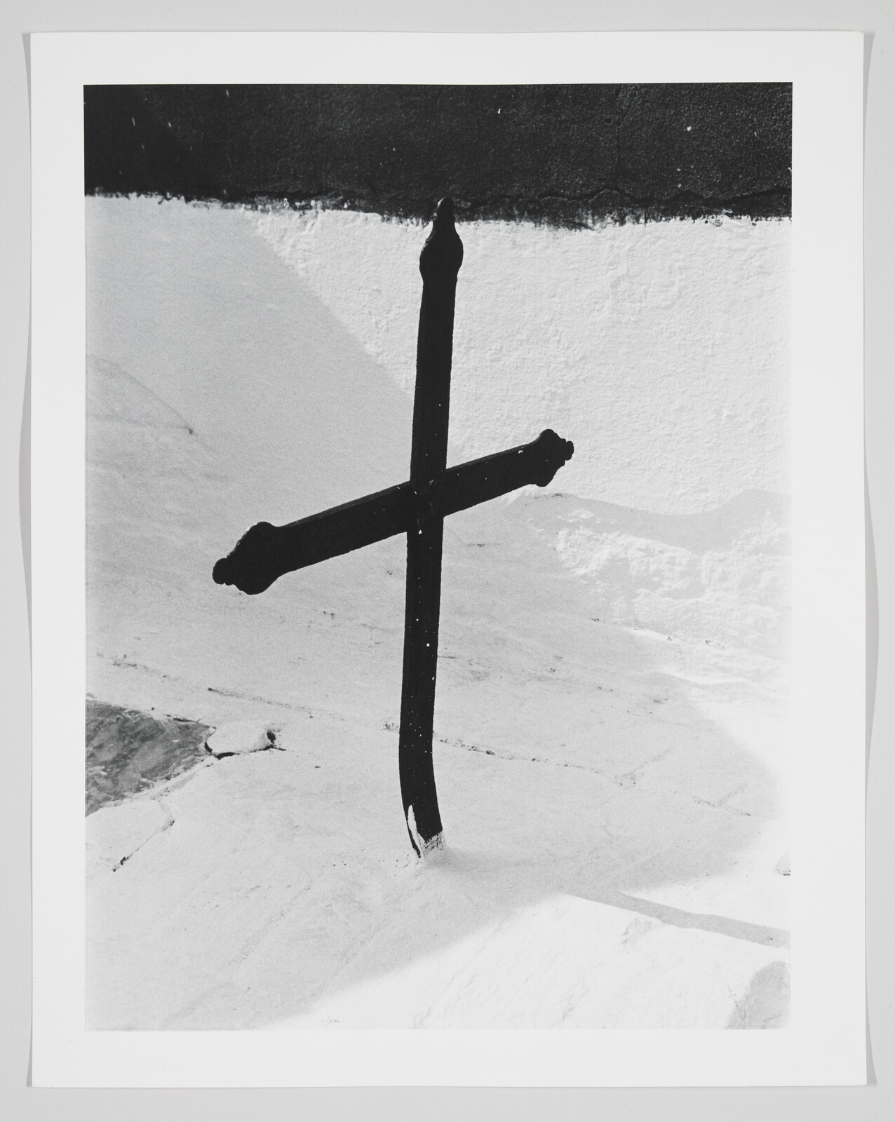 A black metal cross leaning in snow casting a long shadow.