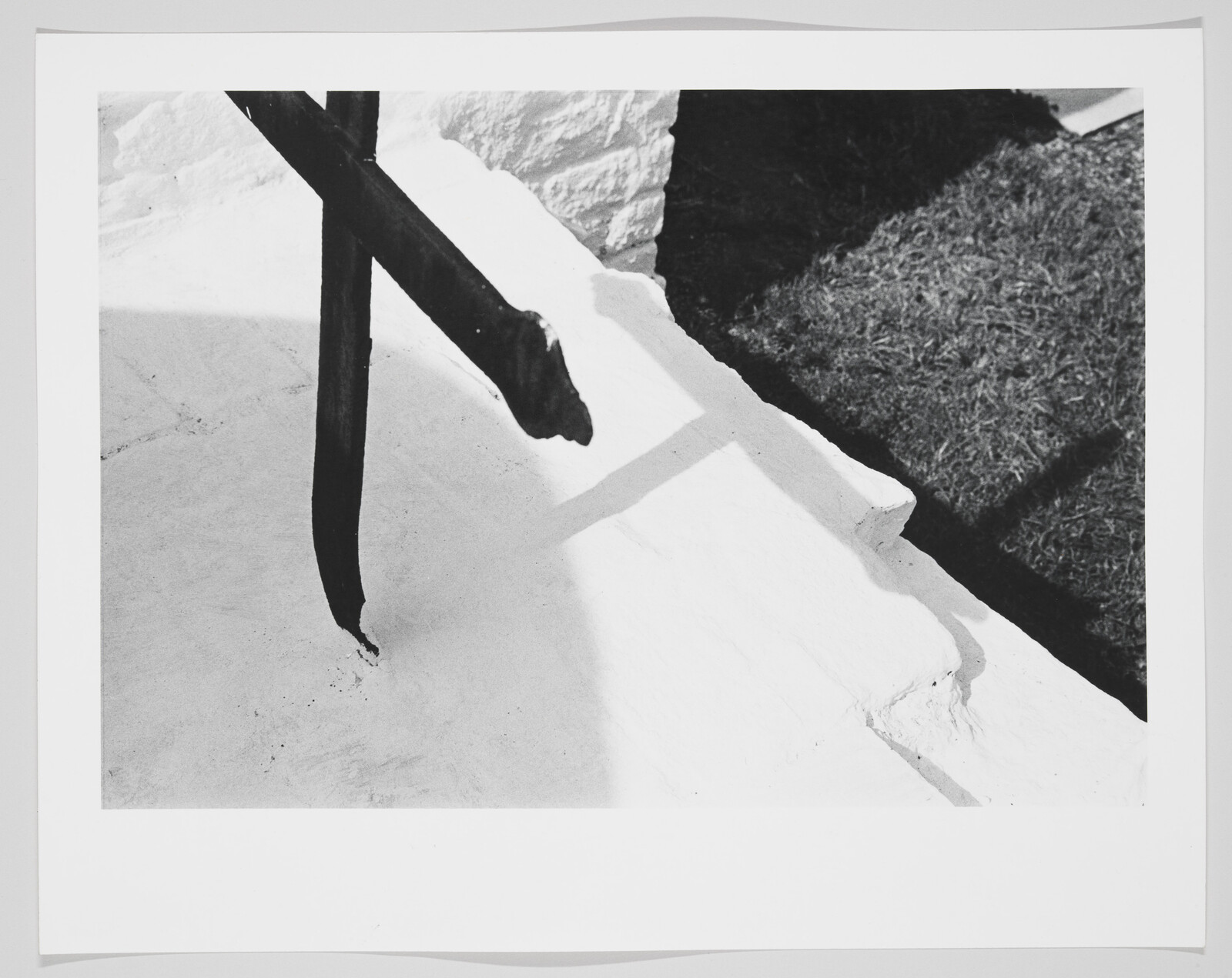 Black metal railing casts a shadow over a white concrete ledge beside a patch of grass.
