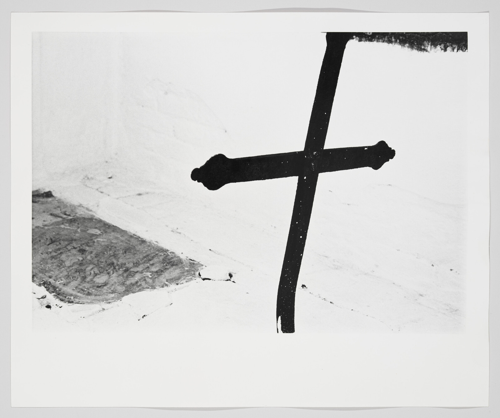 A black iron cross-shaped railing stands against a white textured wall and floor.