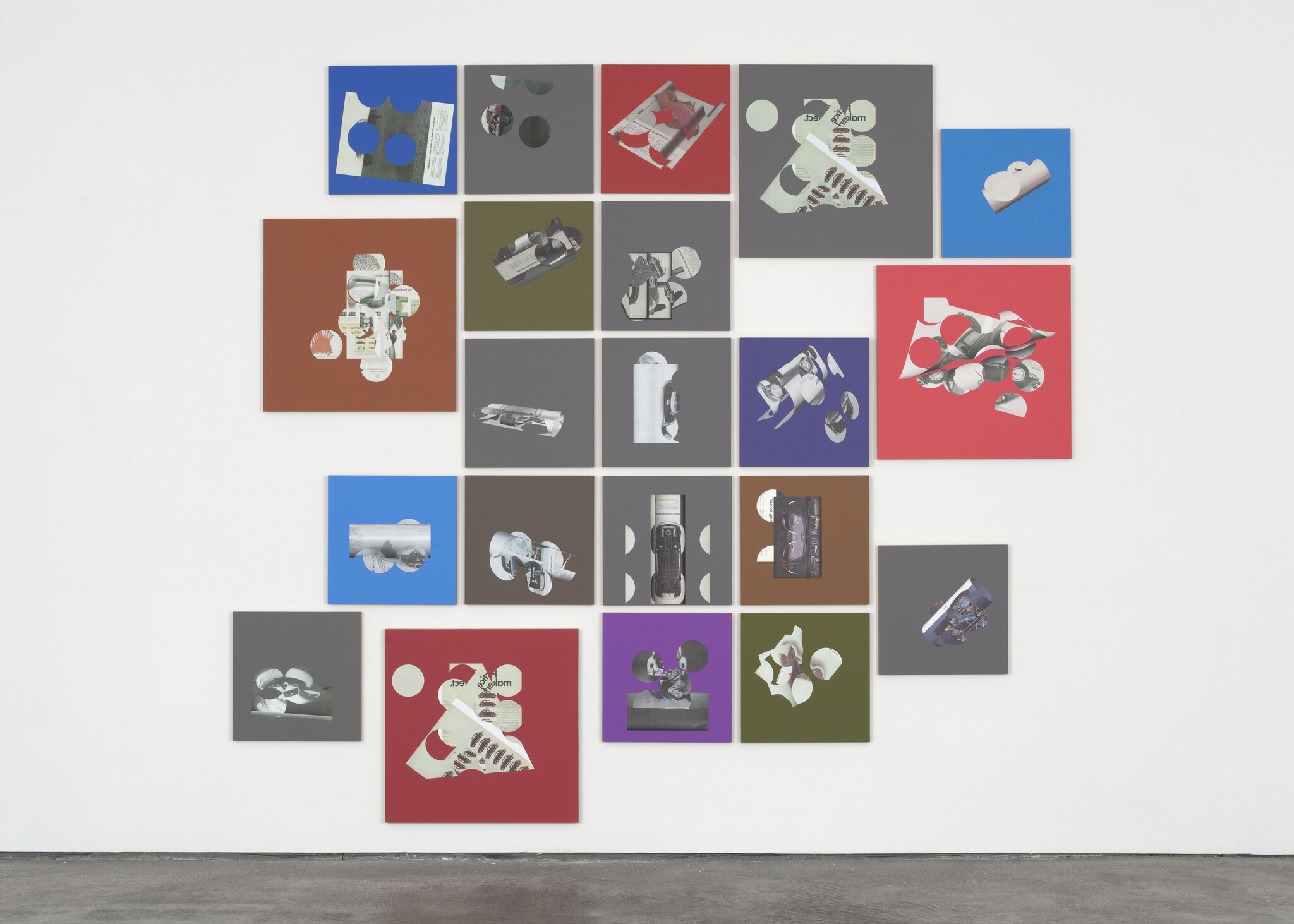 A gallery wall featuring a grid of square and rectangular panels in various solid colors, each displaying a different monochromatic image of objects and shapes that appear to be related to space exploration, such as satellites, rockets, and other equipment. The installation presents a modern, artistic interpretation of space technology.