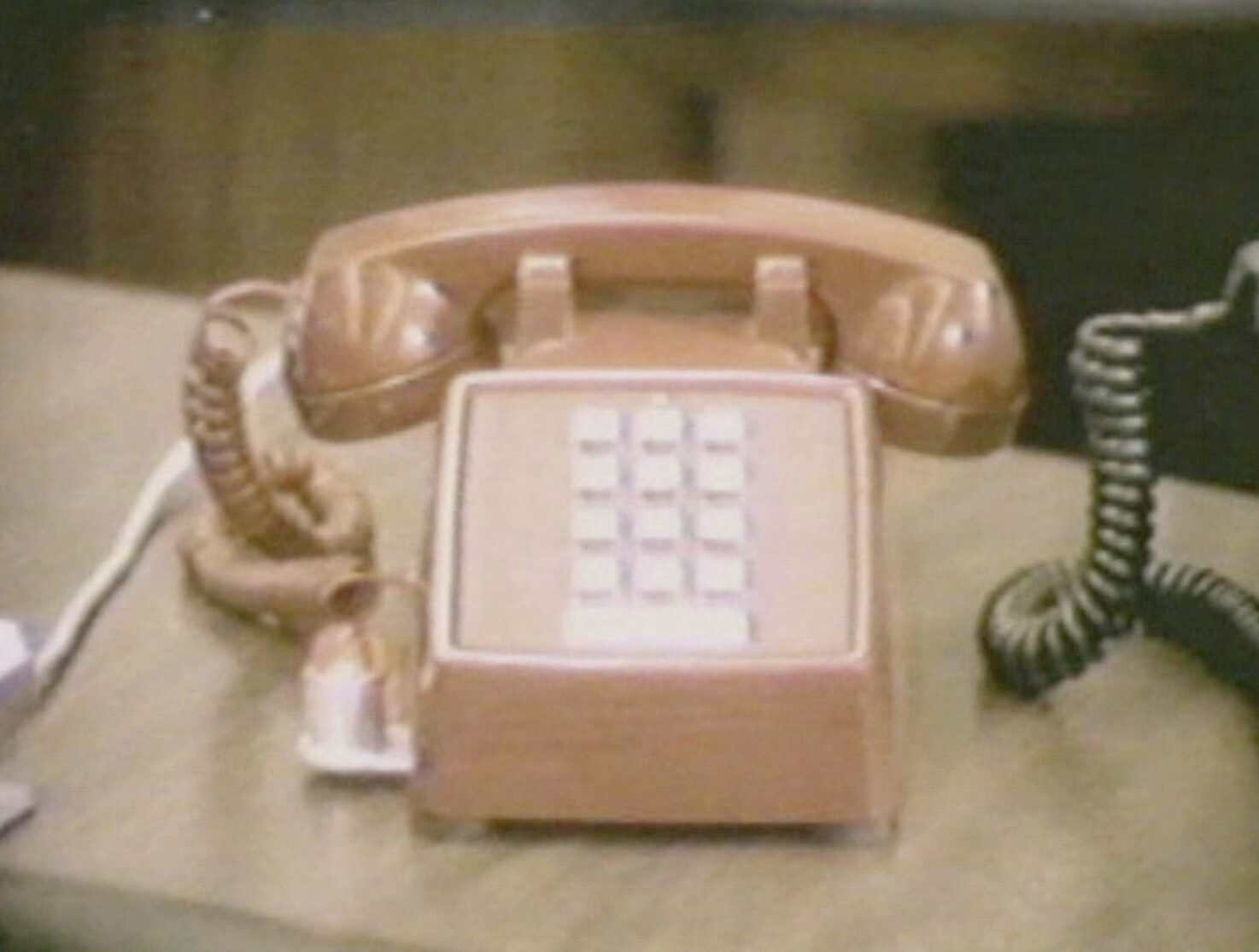 A vintage push-button desk telephone with coiled handset cords resting on a wooden table.