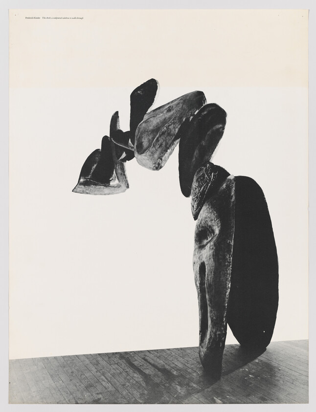 Tall abstract stacked forms form an arch over a wooden floor, casting a shadow.