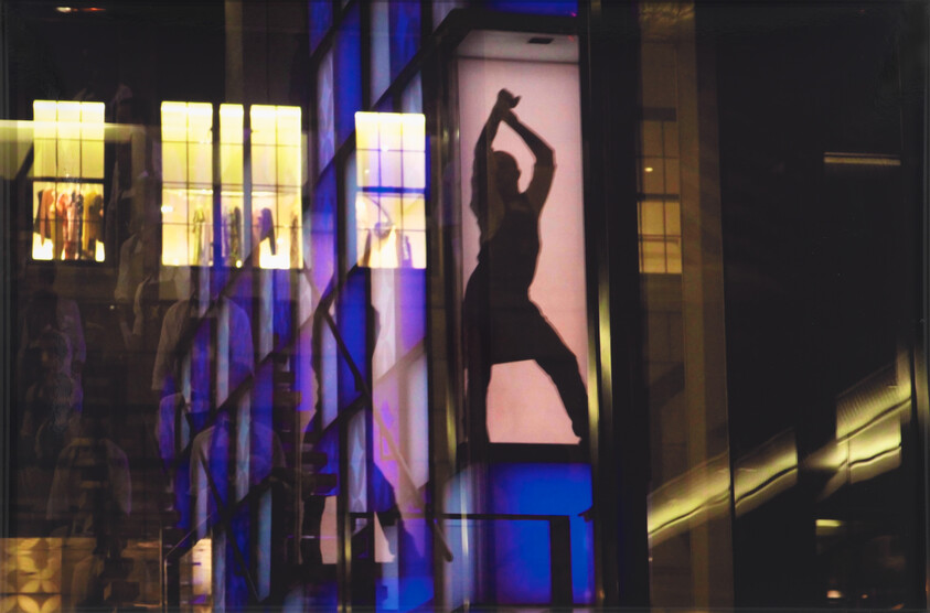 Silhouette of a person striking a dramatic dance pose inside a brightly lit storefront display.
