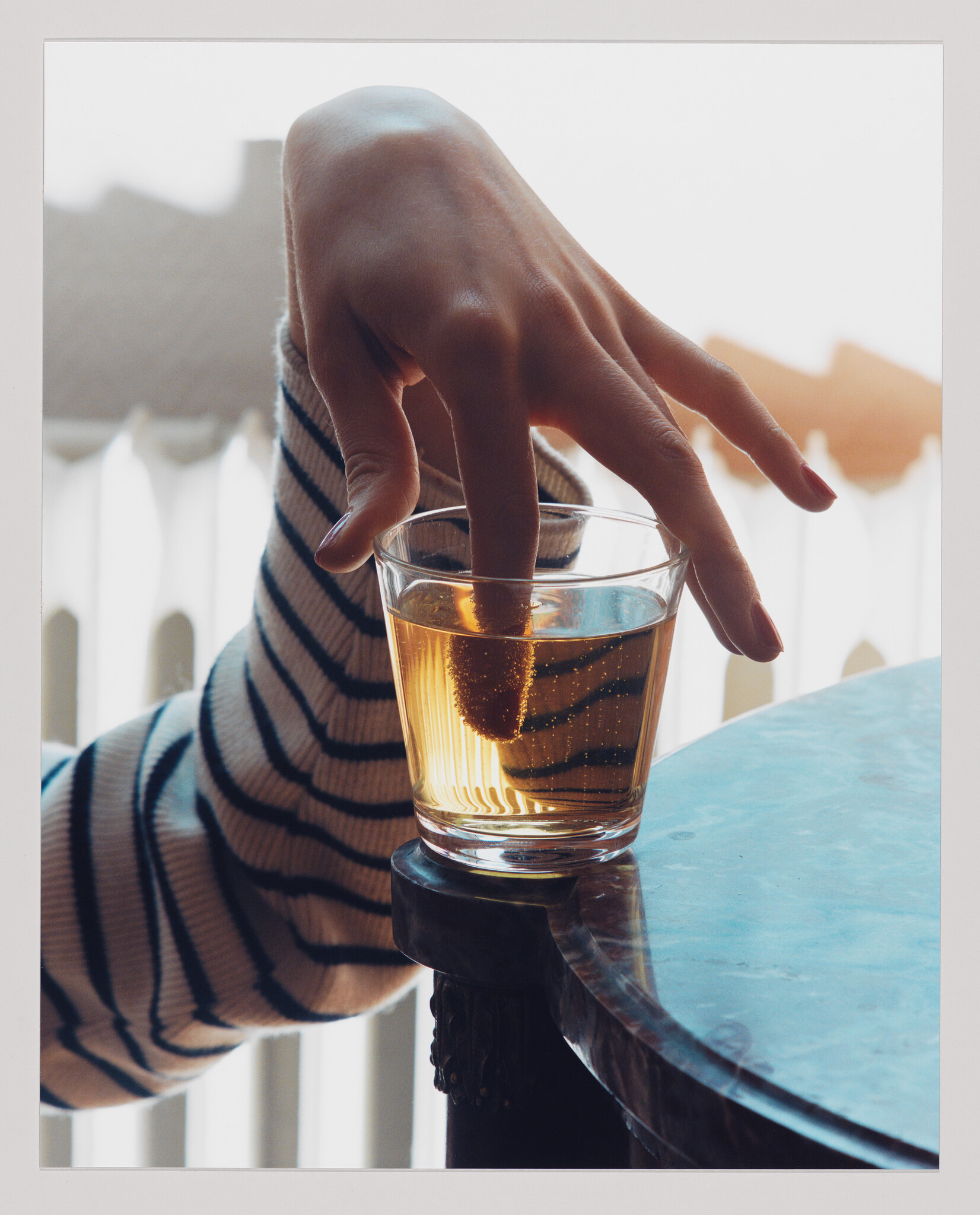 A hand with a striped sleeve dips two fingers into a glass of amber liquid.