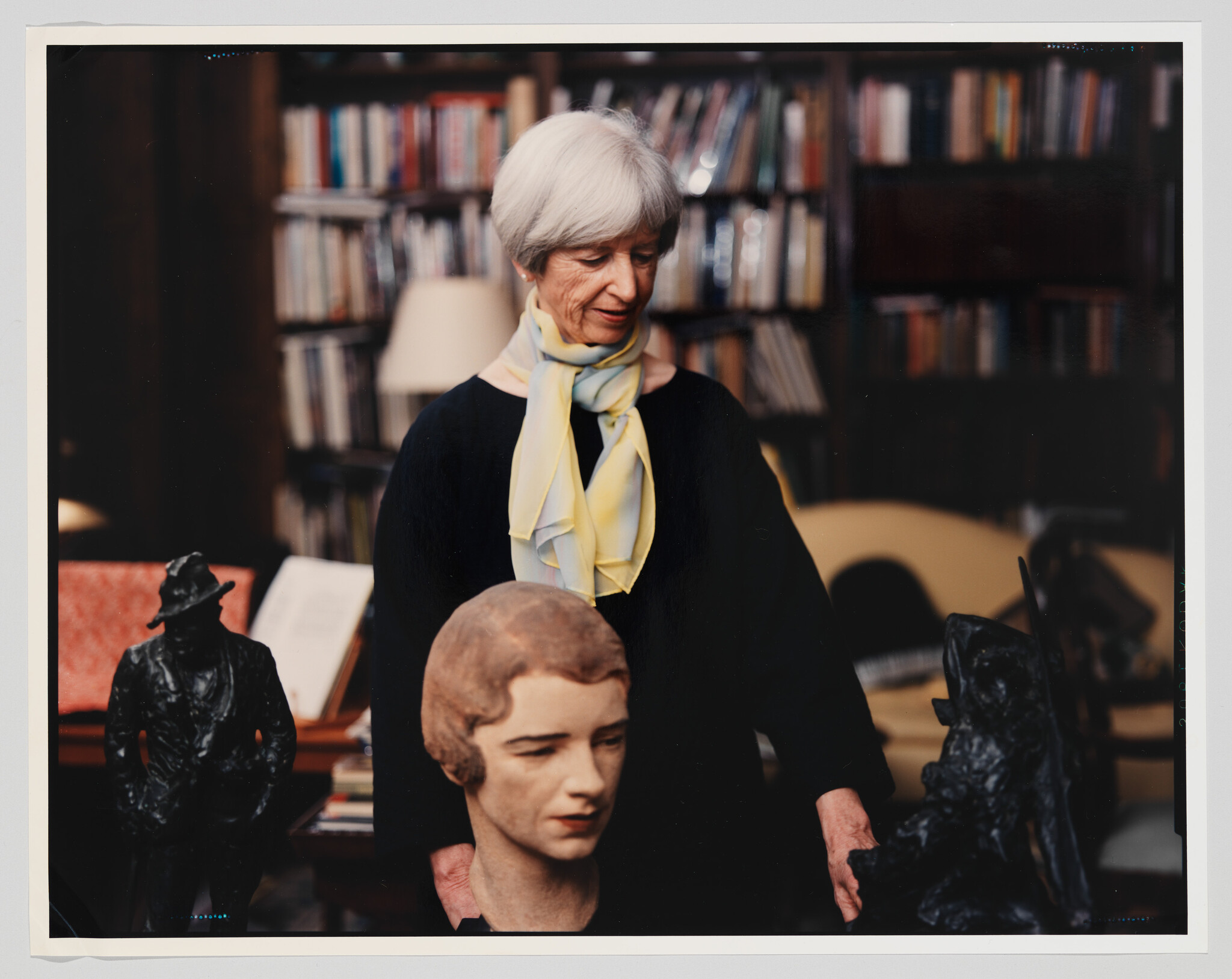 An older woman in a library gently examines several sculpted busts and figurines.