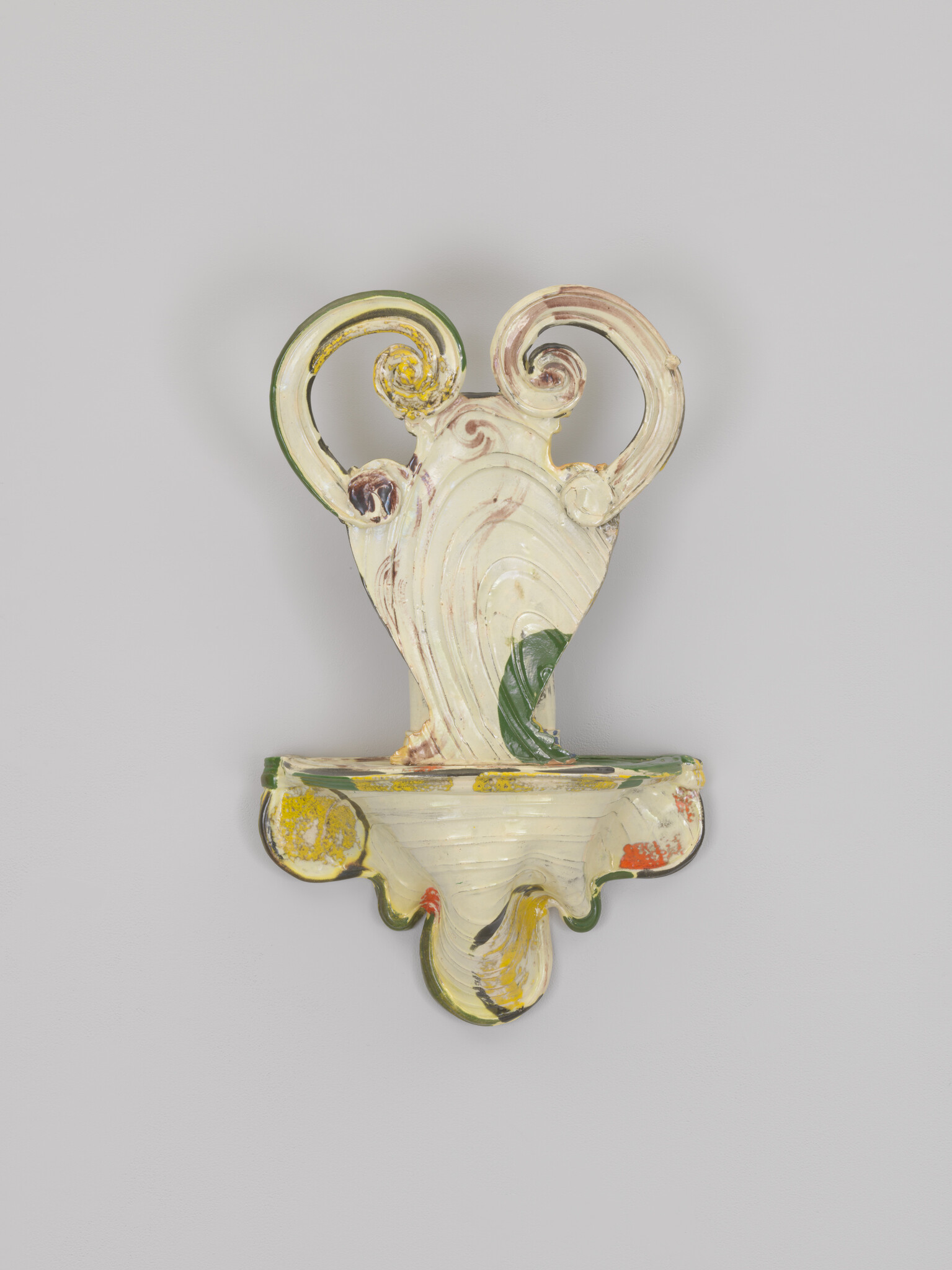 A cream-colored ceramic wall sconce with double curled handles and green and yellow painted accents.