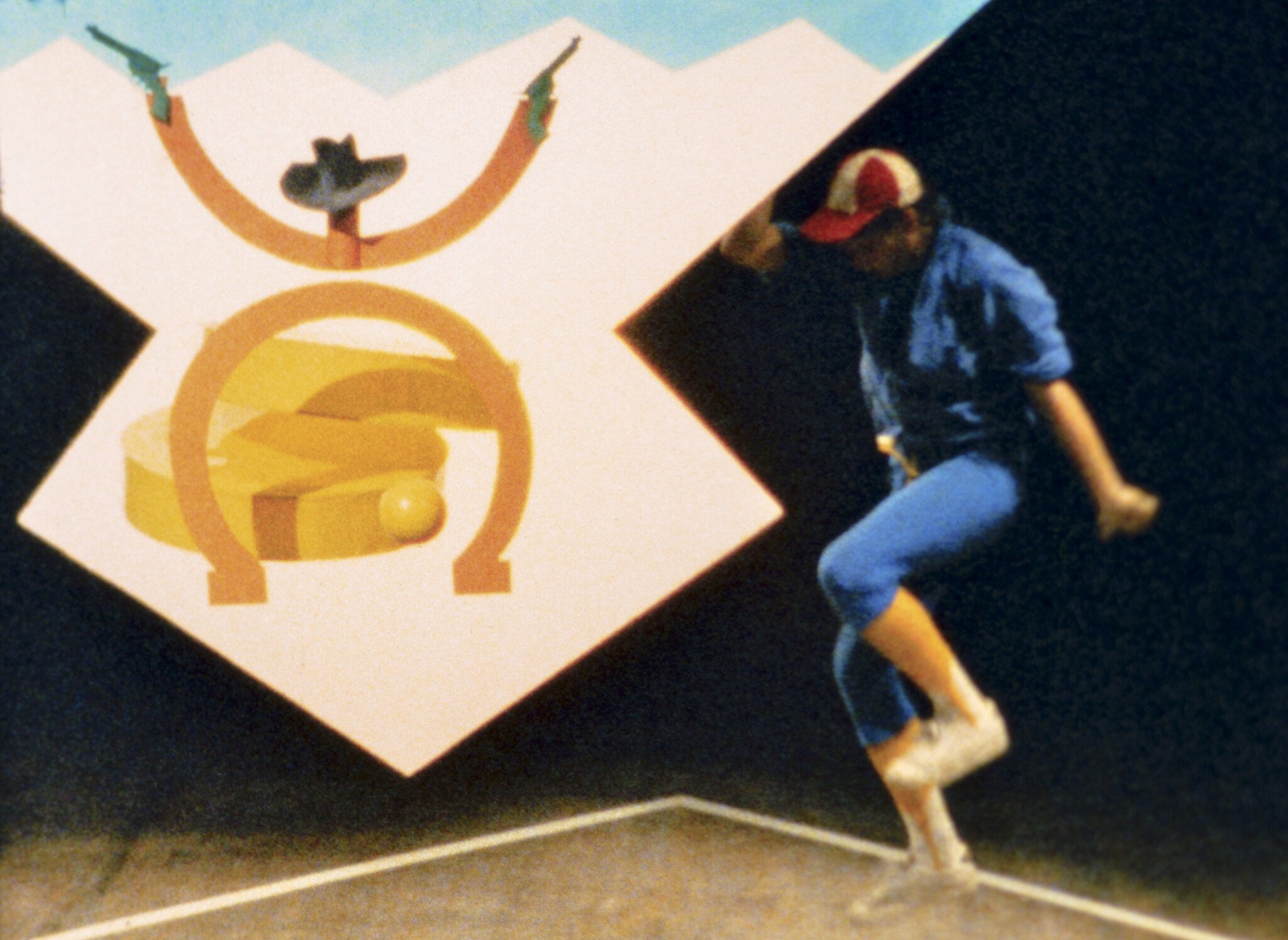 A person in a baseball cap and blue outfit dances on one foot beside a cowboy logo.