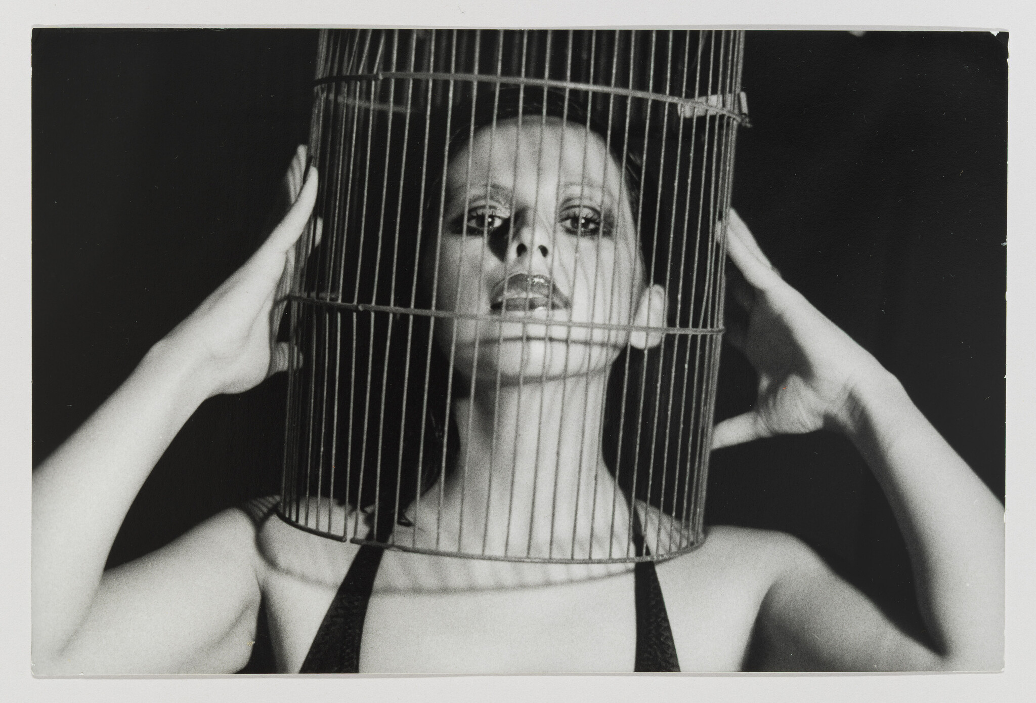 Woman holds a birdcage over her head, face visible through the bars.