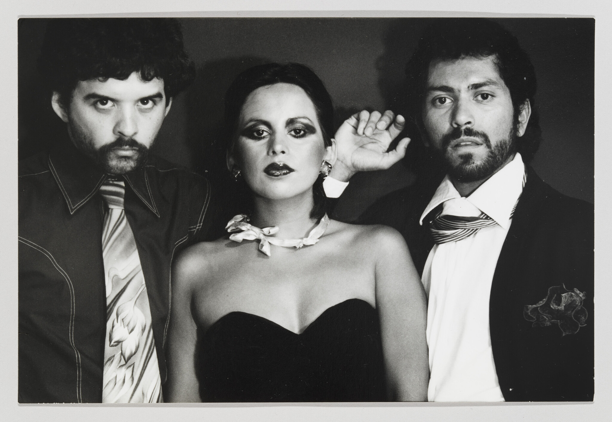 Woman in a strapless dress poses confidently between two serious men in suits.