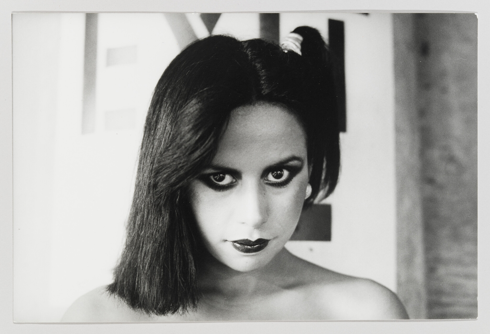 A woman with smudged eyeliner and a single pigtail stares directly ahead