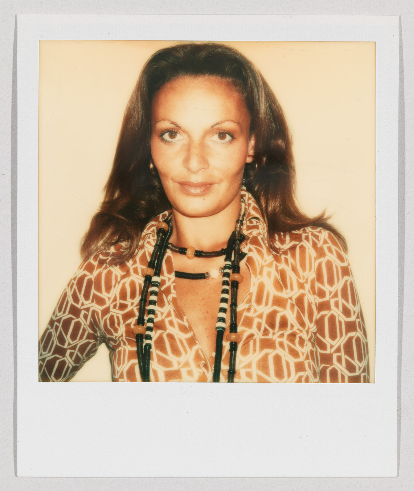 Woman with long brown hair wearing a patterned shirt and beaded necklaces, looking directly at the camera.