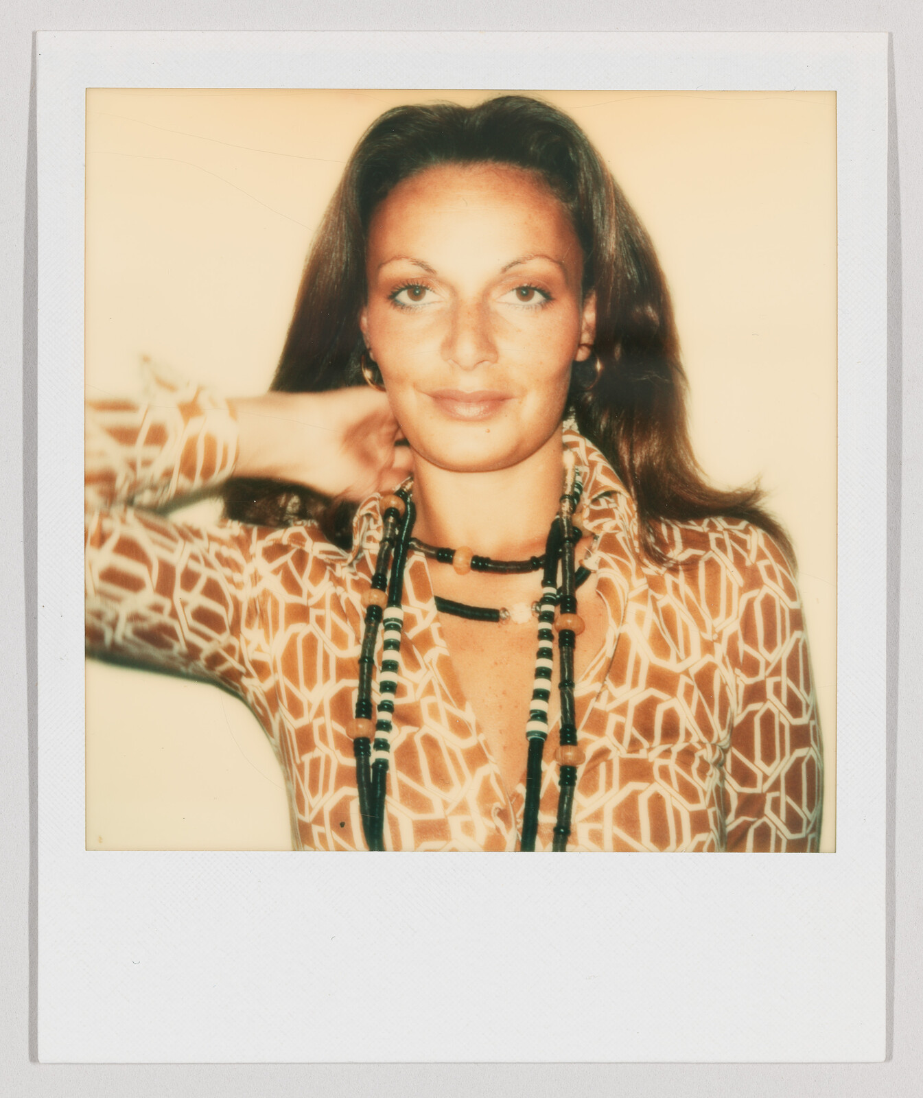 Woman with long brown hair wearing a patterned shirt and beaded necklaces, looking at the camera.
