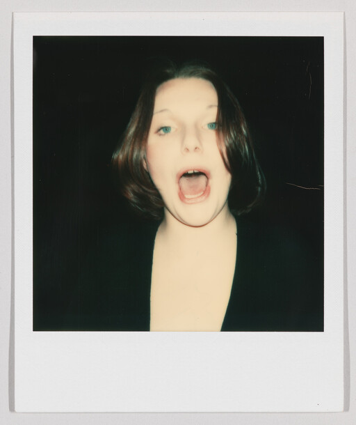 Young woman with short hair faces the camera with her mouth wide open as if shouting.