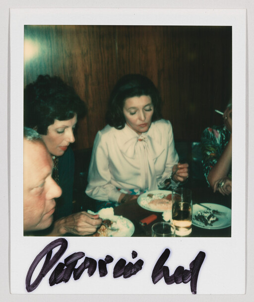 Three people sit at a table while a woman in a white blouse eats dessert.