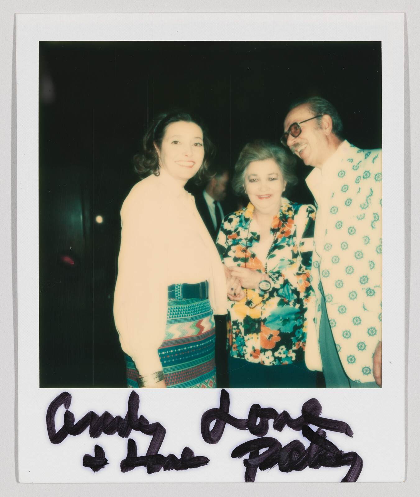 Three adults stand together smiling, with handwritten text at the bottom reading “Andy Love & Hugs Patsy.”