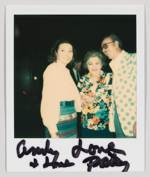 Three smiling adults stand close together, two women holding hands while a man laughs beside them.
