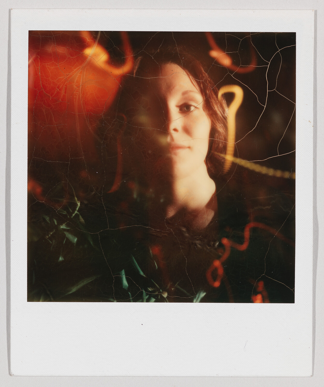 A person with long hair looks at the camera, half of their face is in shadow with colorful lights behind.